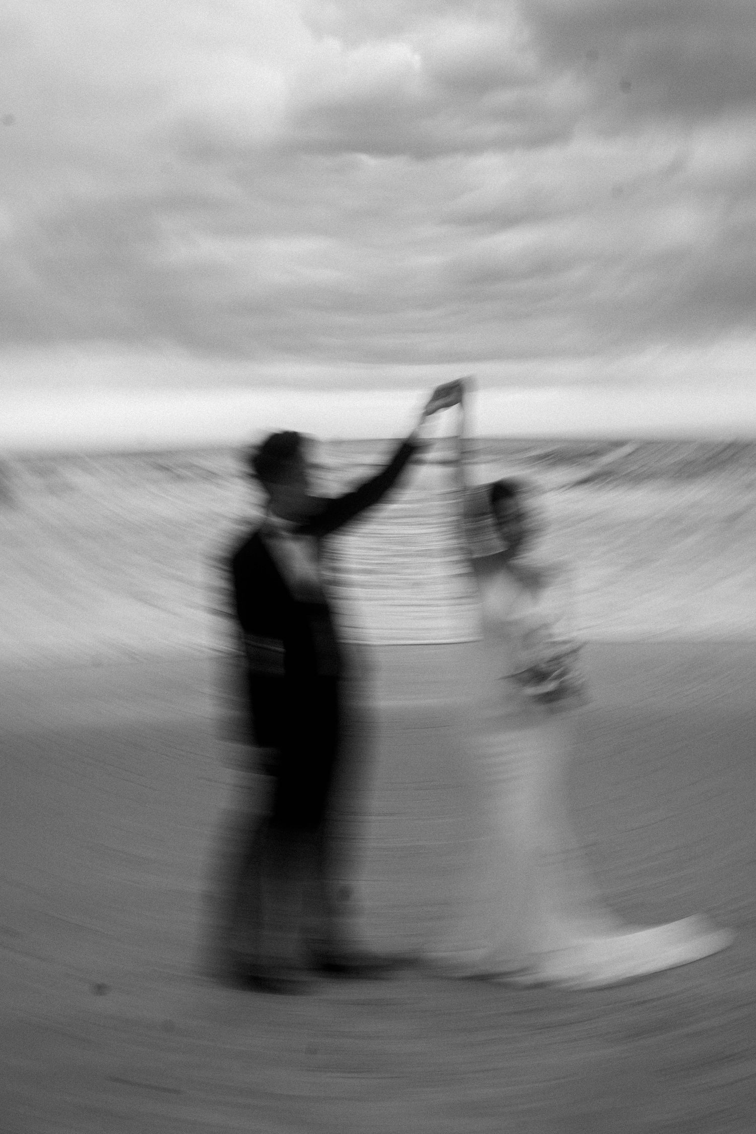 Blurry black and white photo sequence shows silhouetted figures moving across a curved surface in an artistic motion study.