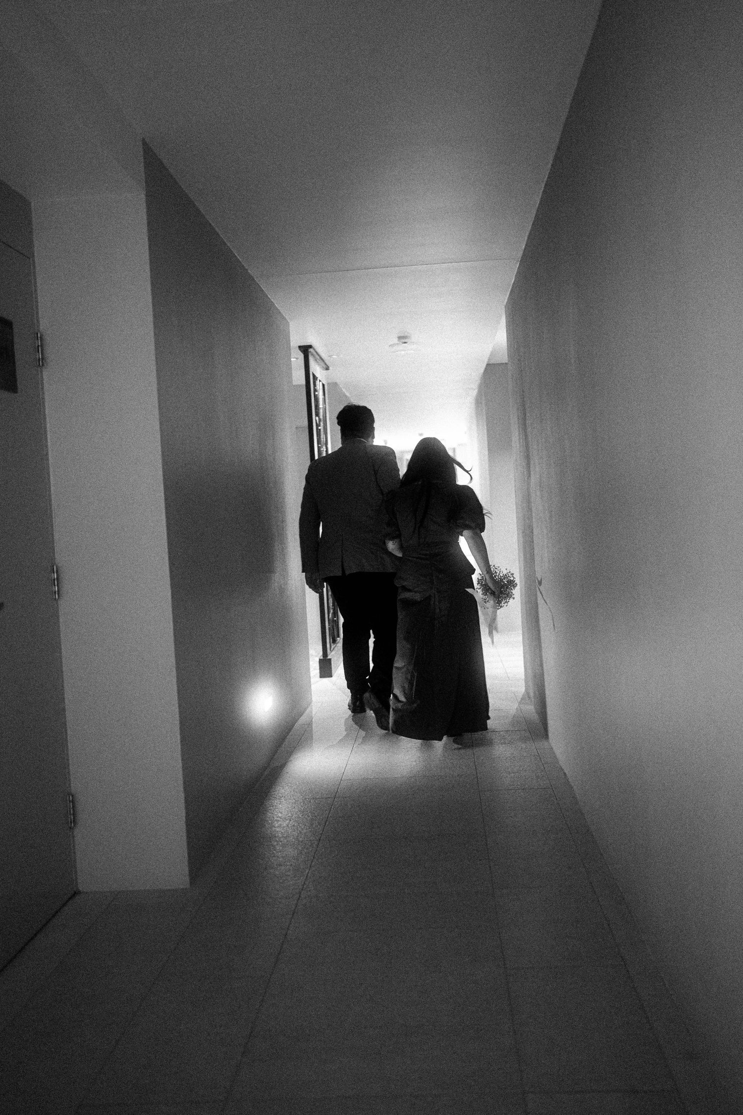 Dark and moody black and white hallway sequence showing silhouettes of figures walking through minimalist interior spaces.