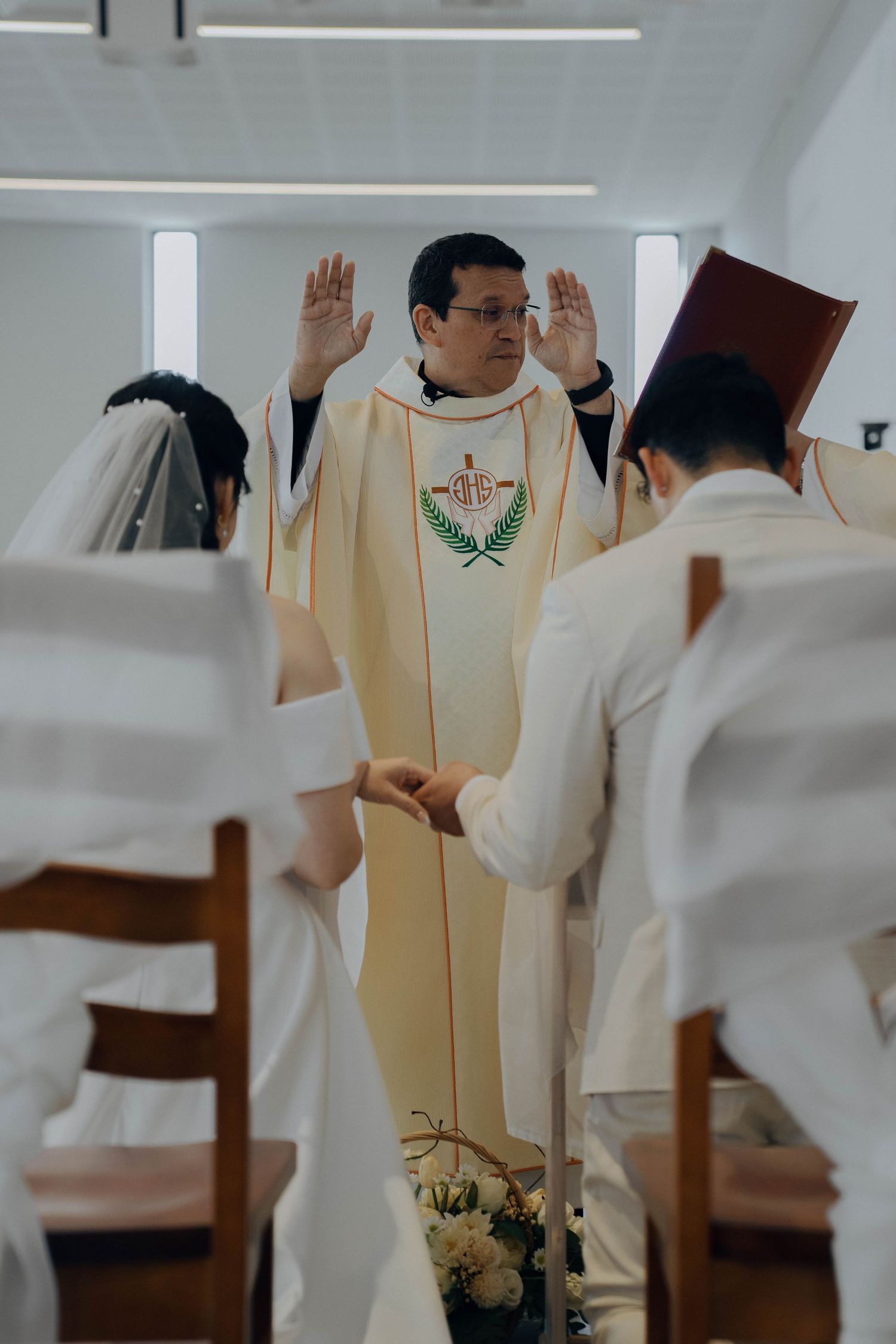 A priest in cream-colored vestments raises his arms during a Catholic mass ceremony.