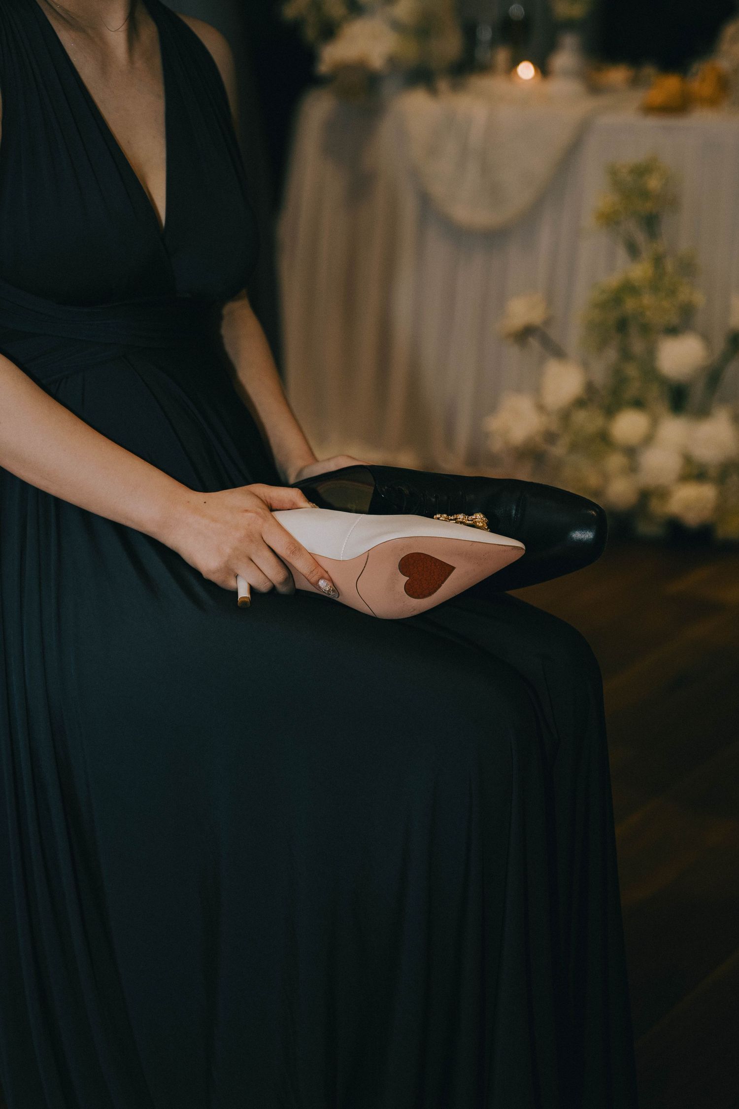 A person in a black dress holds a small heart-shaped object against a dark background in an intimate setting.