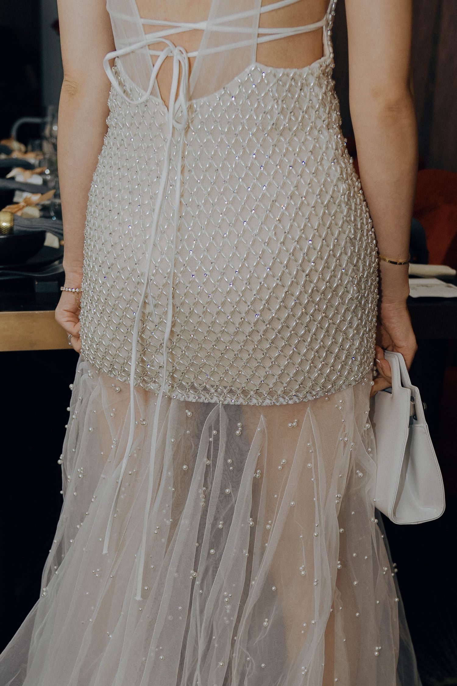 Close-up detail of a beaded wedding dress with sheer tulle overlay and delicate lace-up back design.