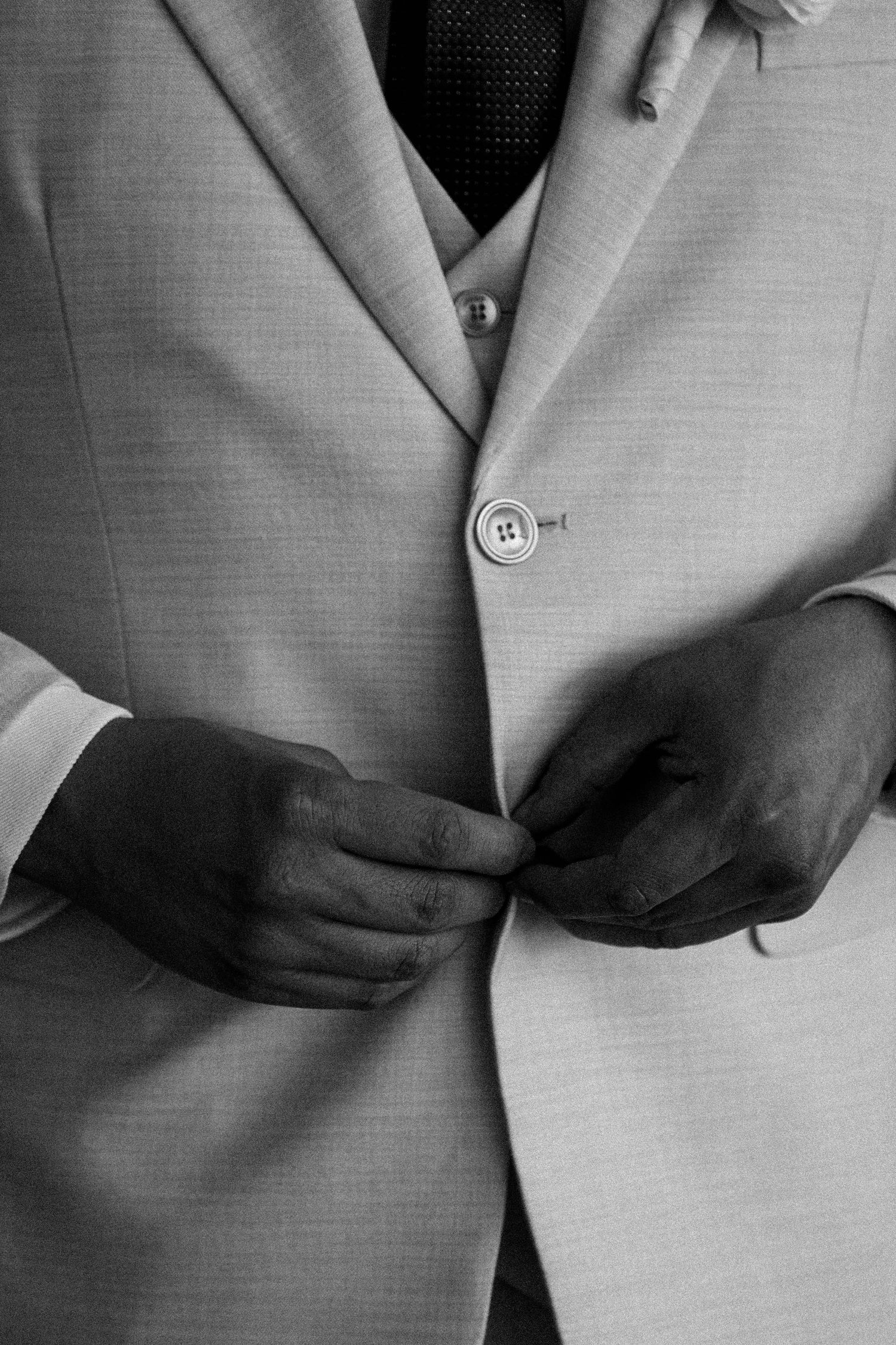 Close-up sequence showing hands buttoning a light colored suit jacket.