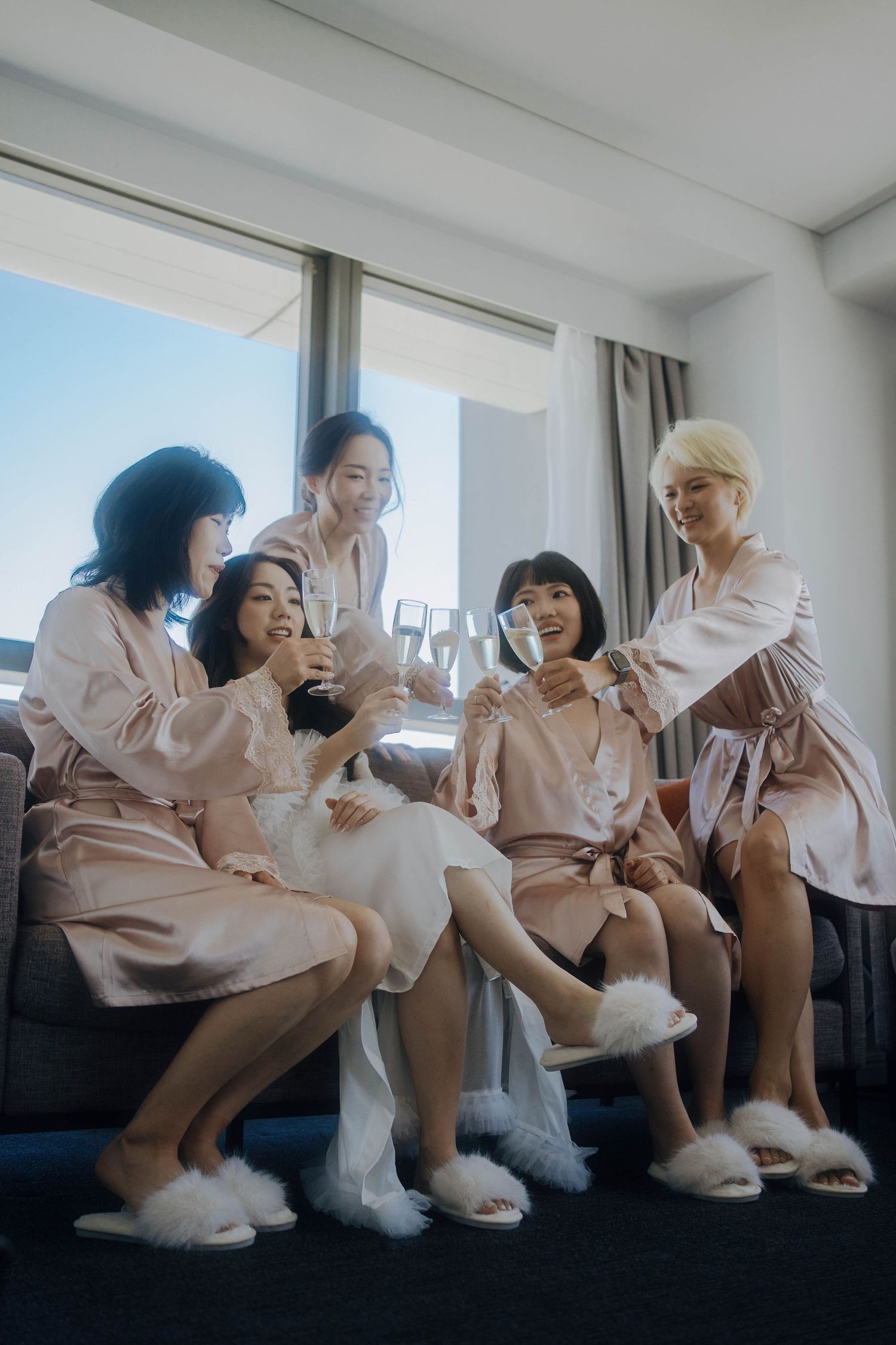 Friends in matching pink robes sitting together on a window ledge during a special occasion.