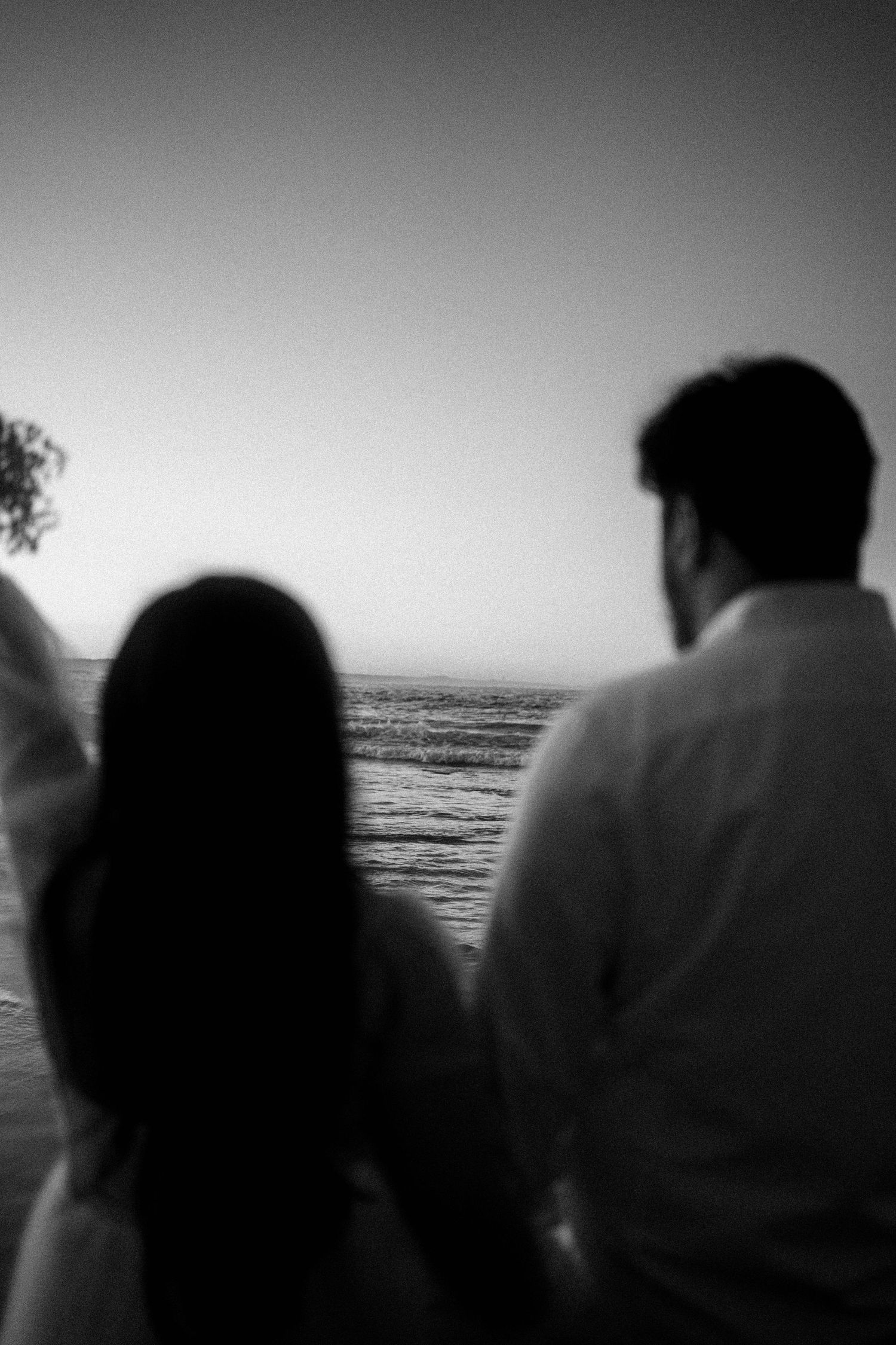A black and white silhouette of a couple looking out at the ocean waves during sunset.