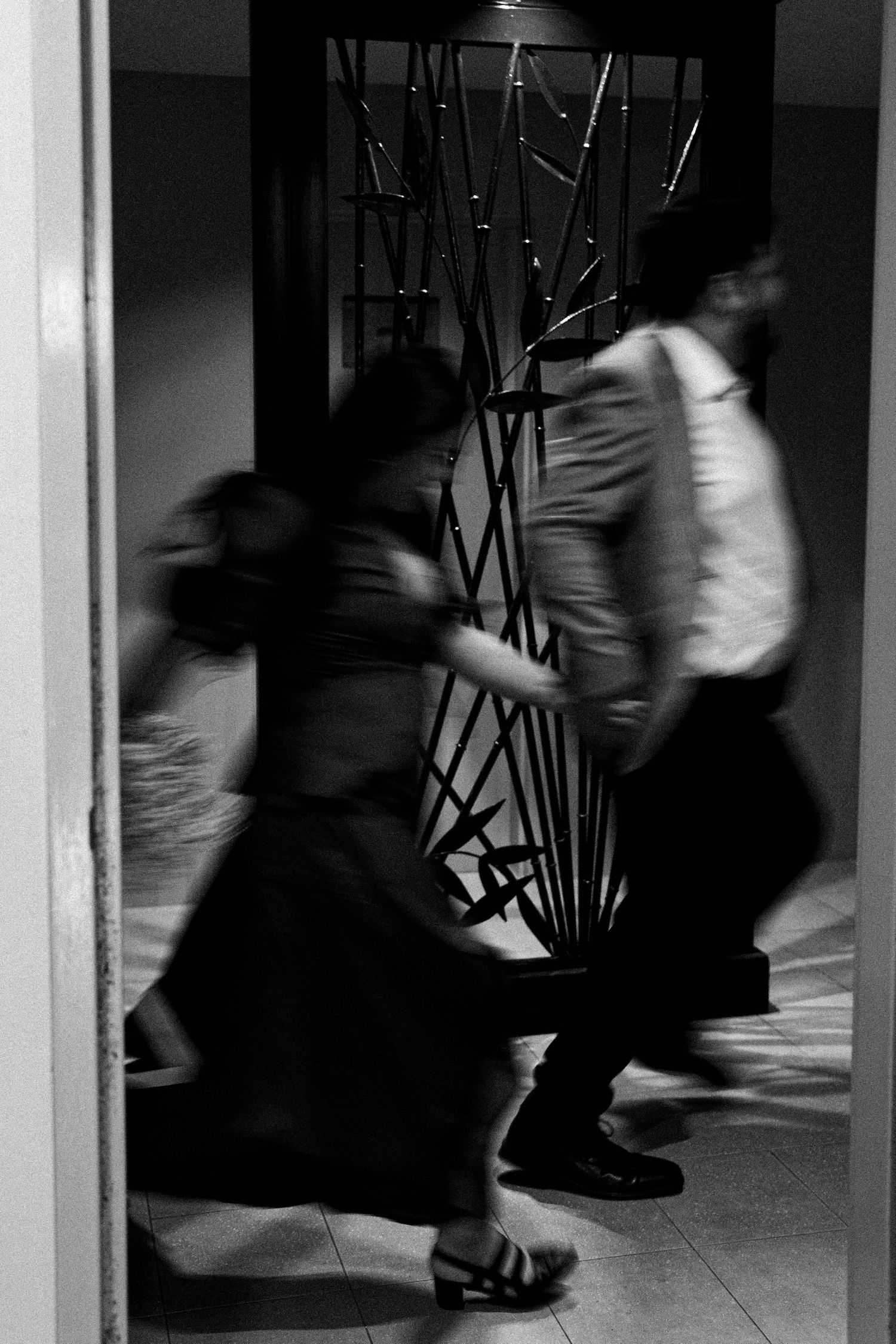Blurred motion of people walking through a dimly lit corridor creates a dynamic black and white composition.