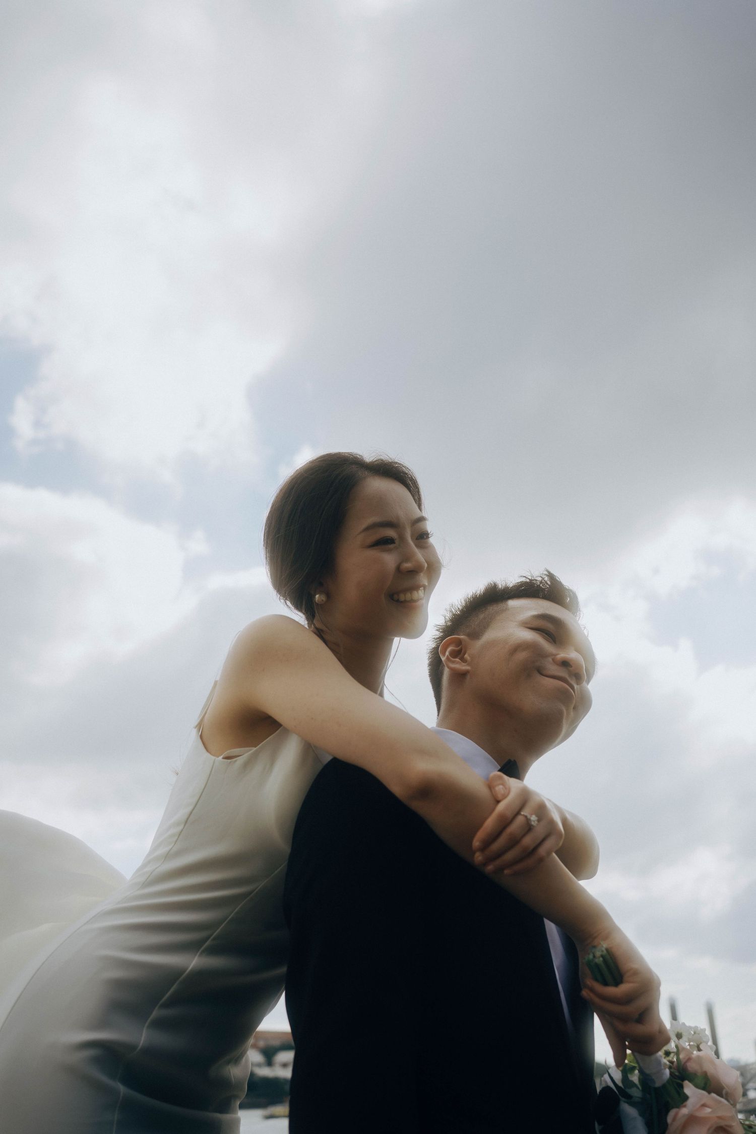 A couple embraces and laughs together against a cloudy sky in a series of candid moments.
