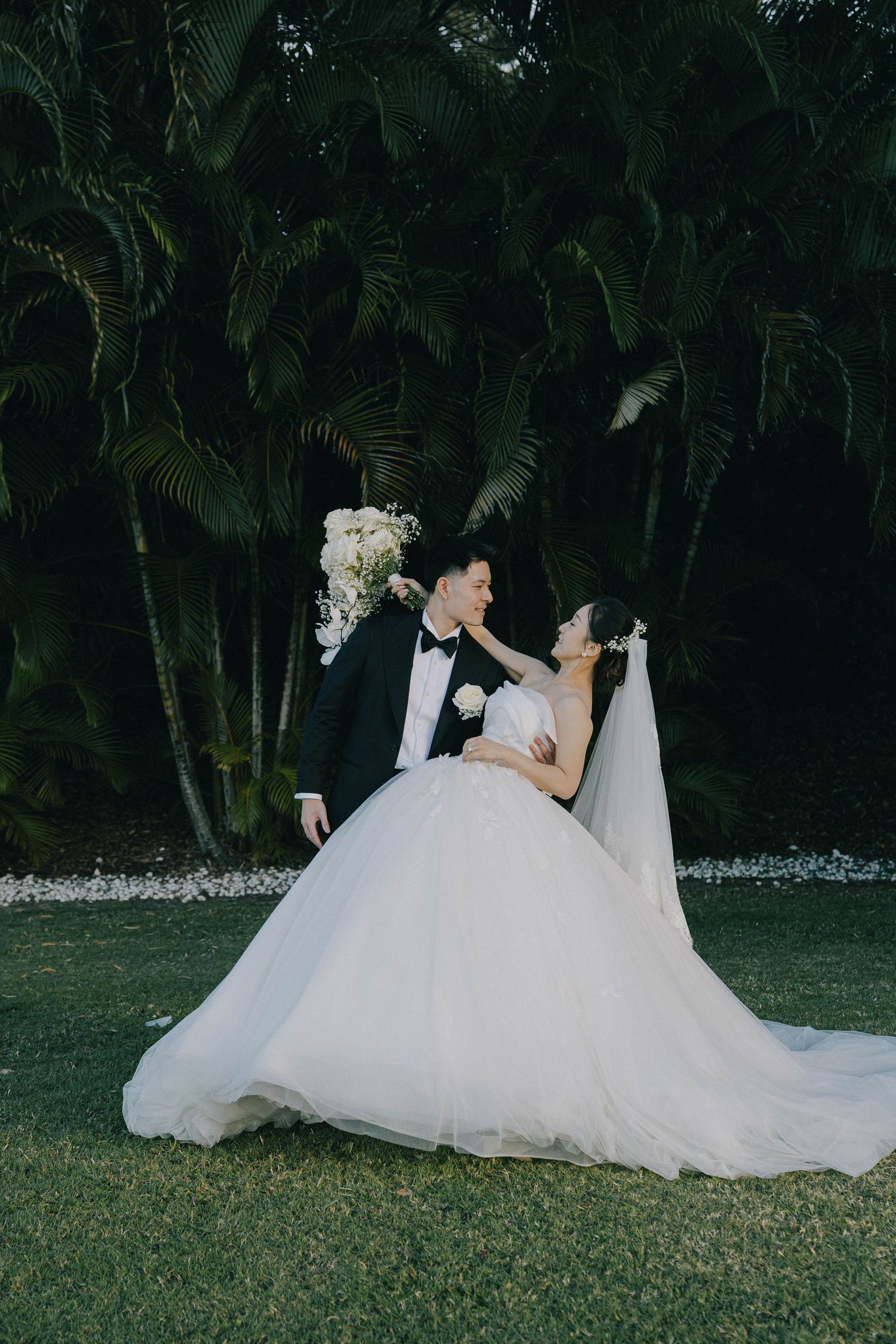 A romantic wedding couple dips in an elegant dance pose against a backdrop of lush tropical palm trees.