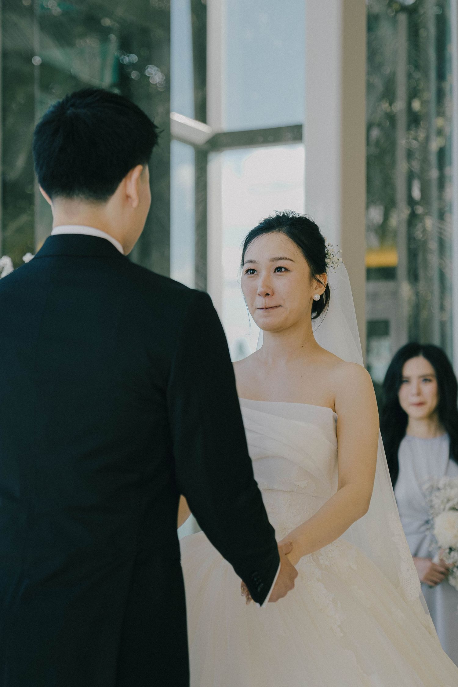 A bride in a white strapless wedding gown stands next to a groom in a black suit in an elegant indoor venue.