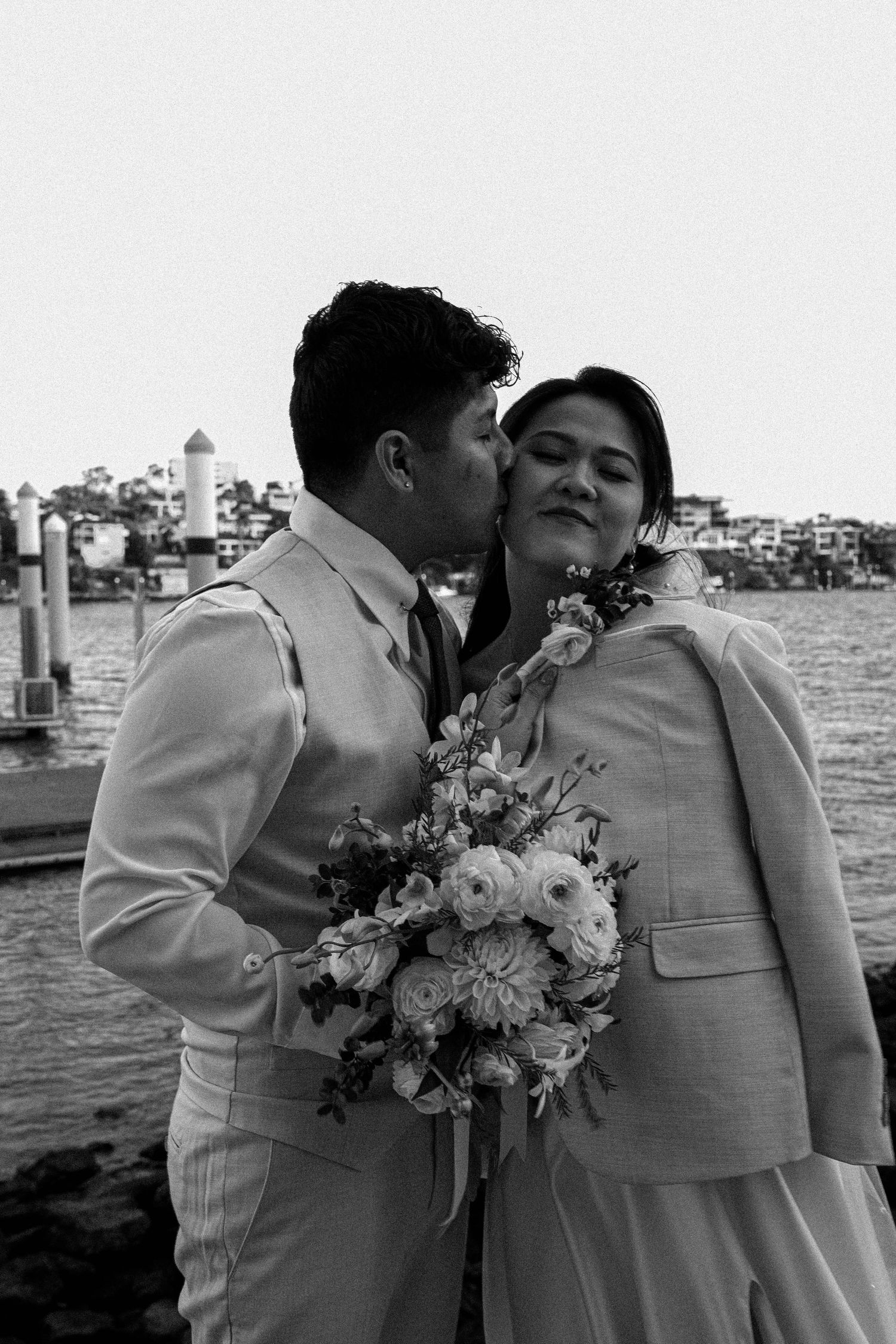 A romantic couple embraces by the waterfront in a series of black and white wedding photos.