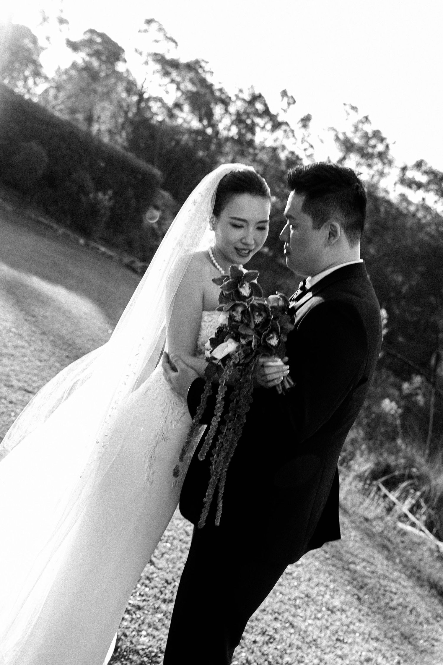 A romantic black and white wedding photo shows a couple sharing an intimate moment outdoors with the bride holding a bouquet.