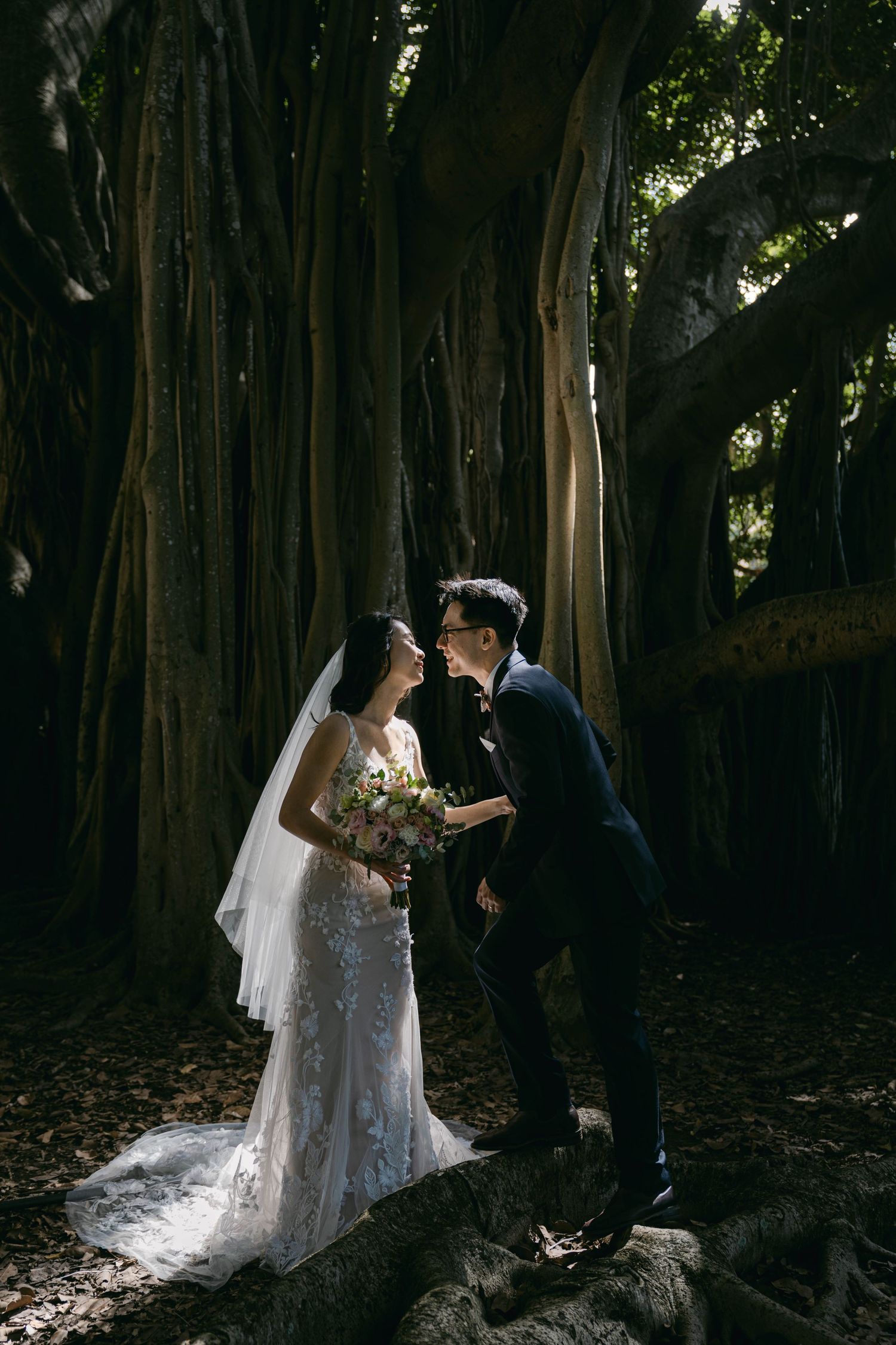 Newlywed couple shares romantic moment under majestic banyan trees in a enchanted forest setting.