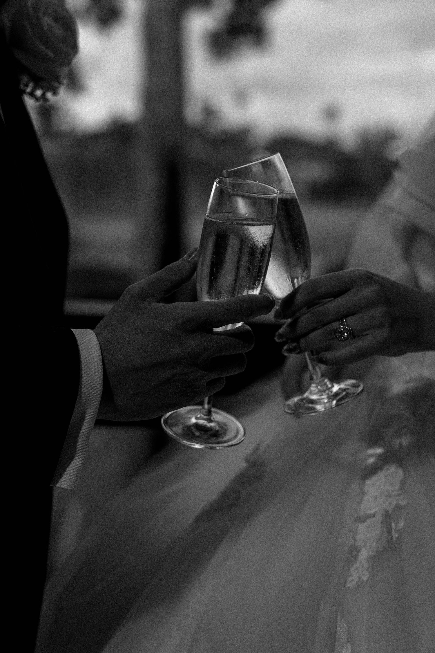 Two hands holding champagne glasses in a toast, captured in black and white with soft lighting and elegant ambiance.
