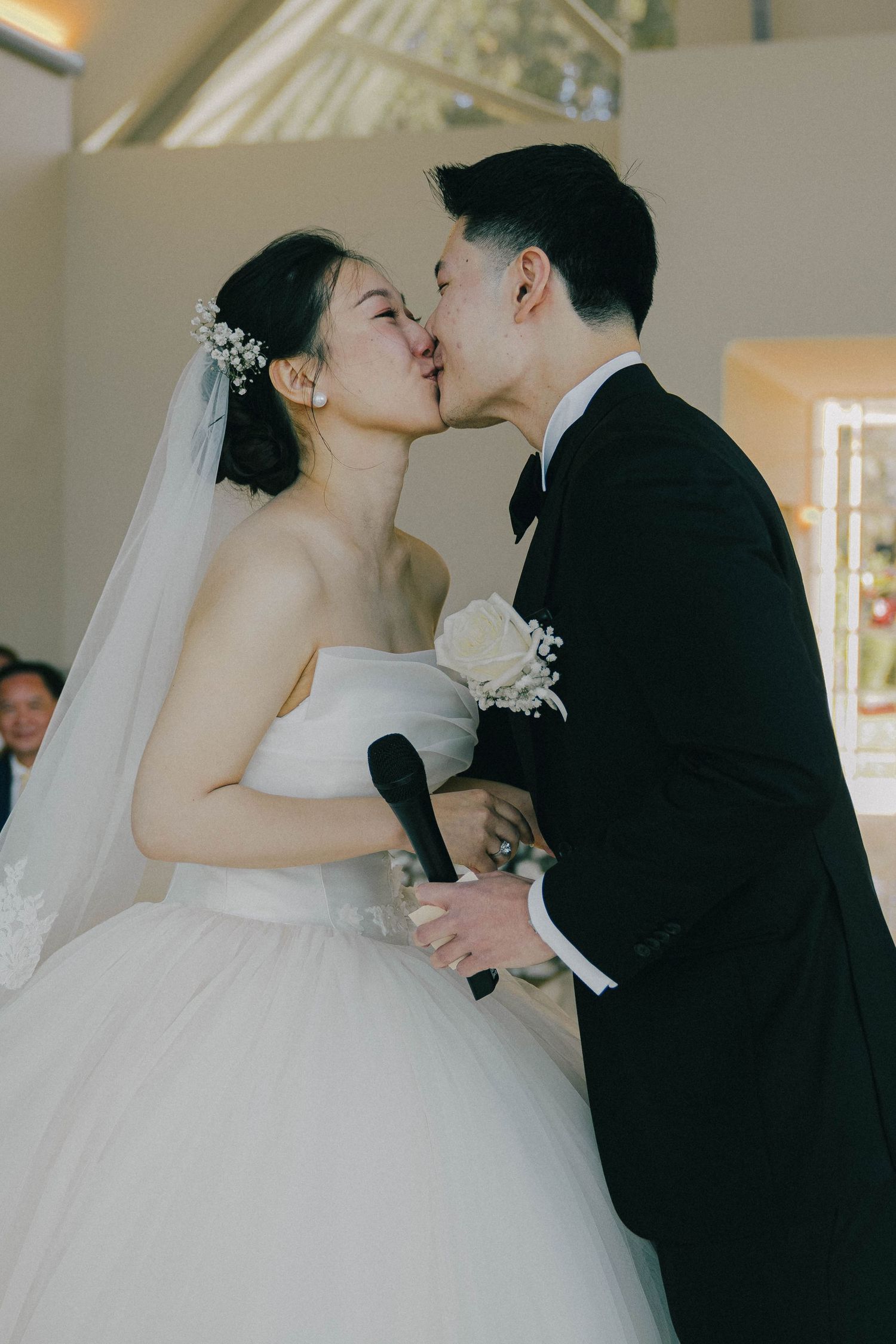 A romantic kiss shared between newlyweds at their wedding ceremony, with the bride in a white ballgown and groom in black suit.