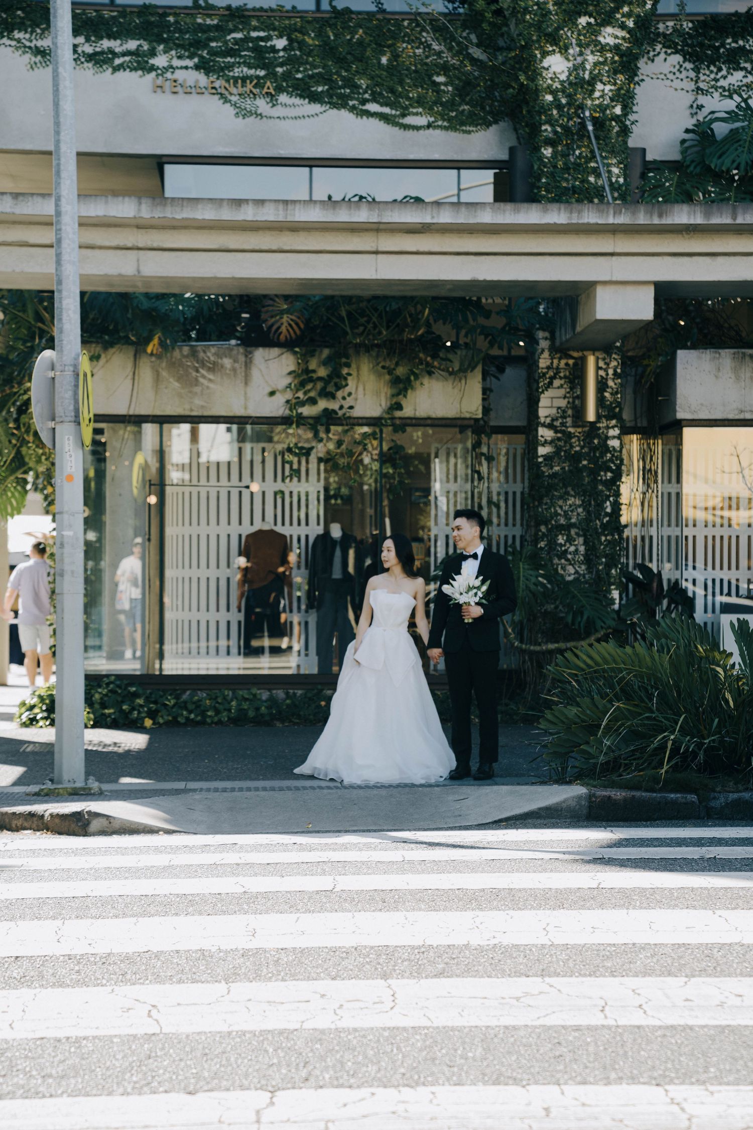 A wedding party walks along a covered outdoor walkway with white columns and greenery in an elegant venue setting.