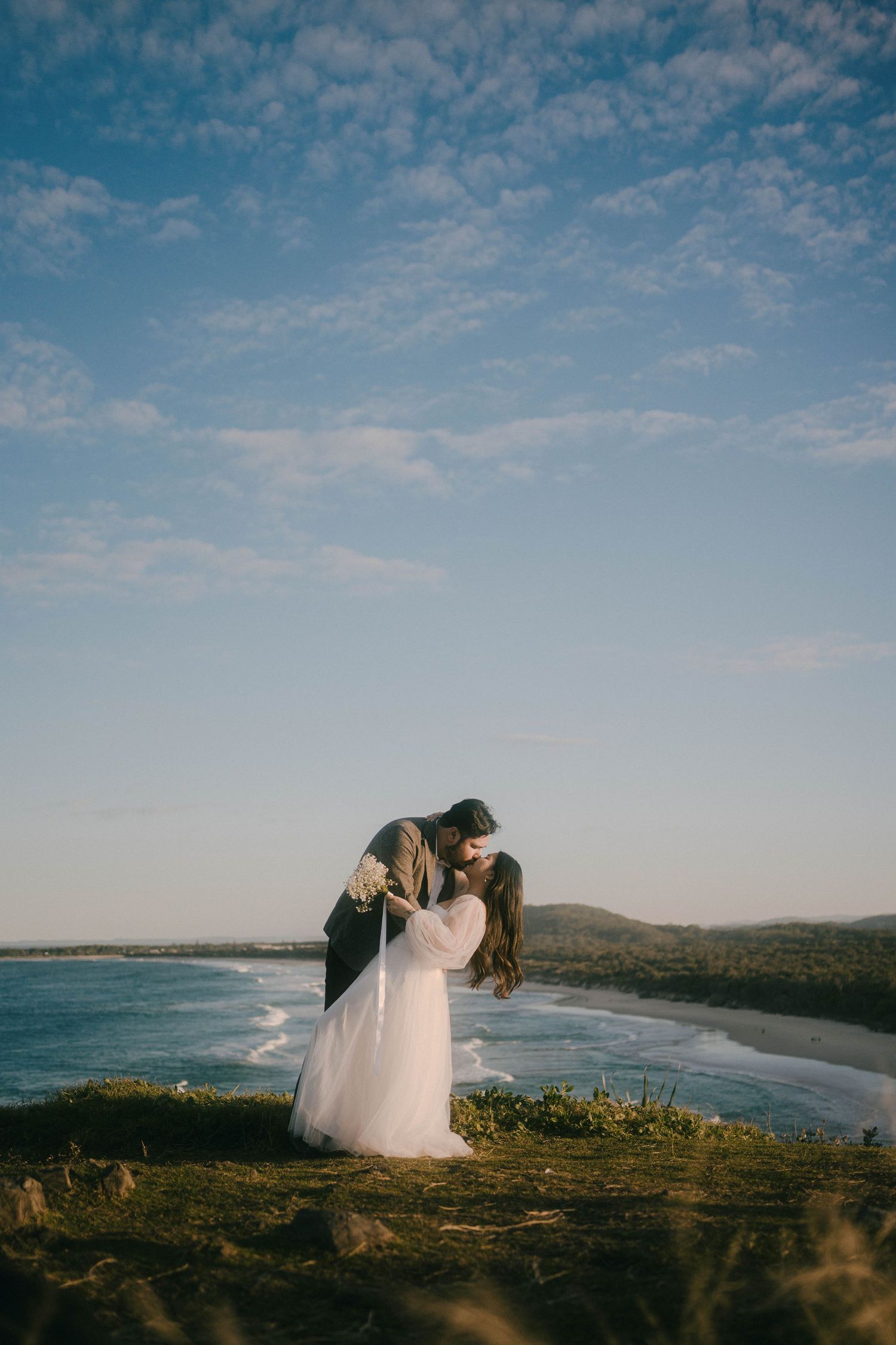 A coastal wedding photoshoot featuring a couple in wedding attire against dramatic ocean views and cliffside landscapes.