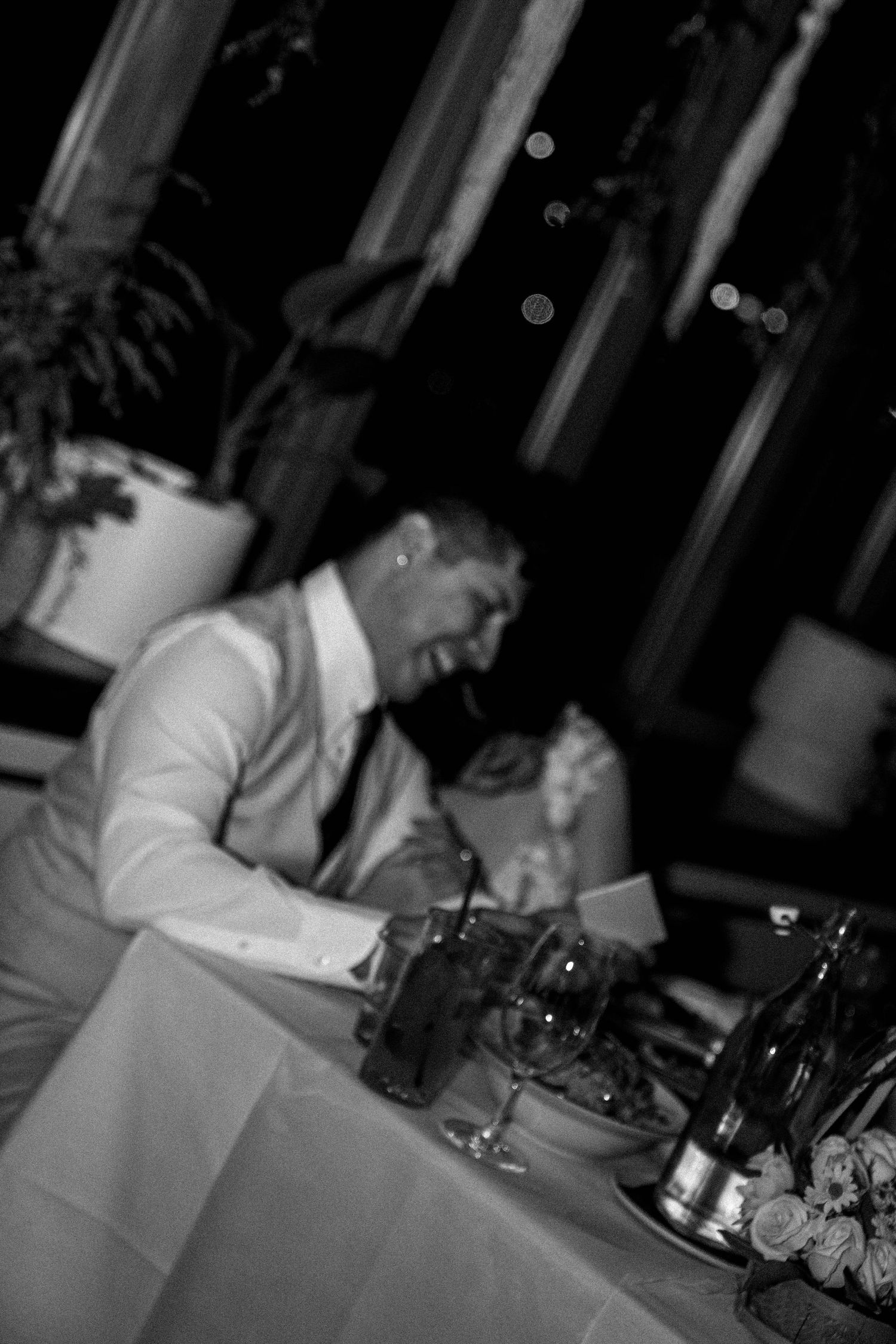 Black and white photo of someone in formal attire seated at an elegant dining table with glassware and table settings.