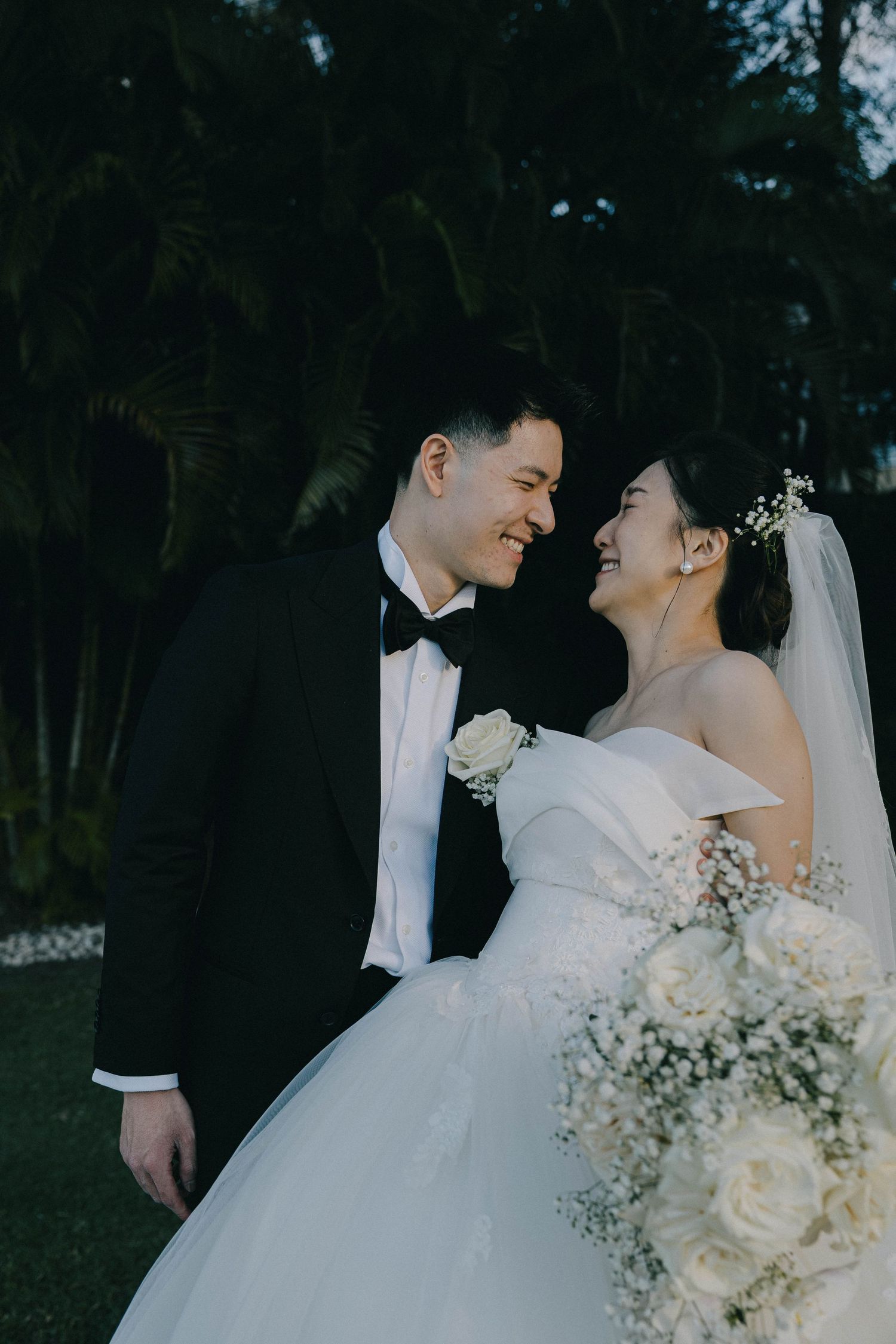 Bride and groom share romantic moments in an outdoor garden setting with white floral bouquet and formal wedding attire.