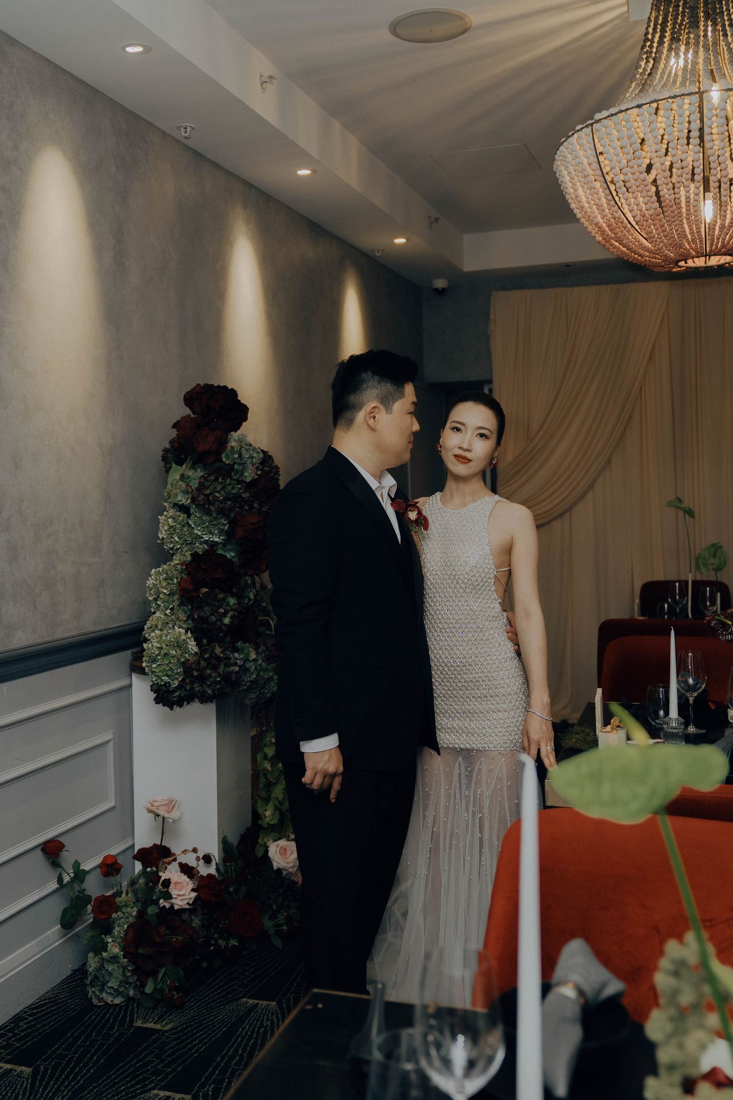 A couple shares a romantic moment in an elegant indoor venue with chandelier lighting and floral decorations.