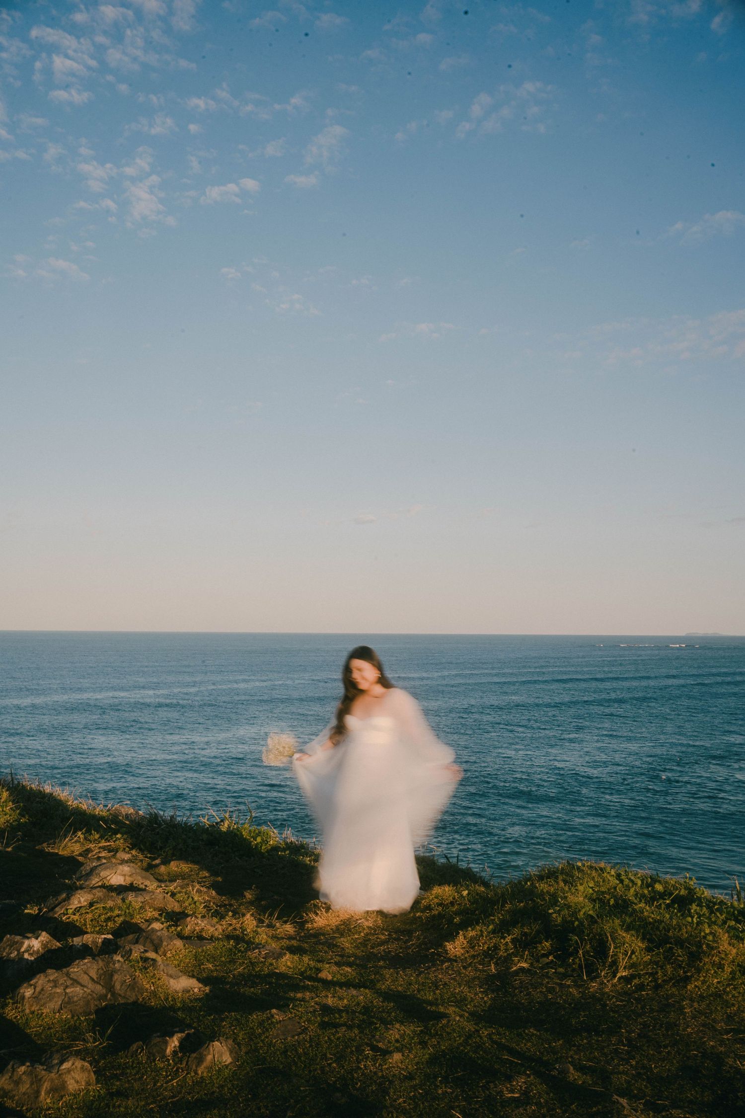 A series of coastal images showing figures in flowing white fabric moving against a blue ocean horizon at sunset.