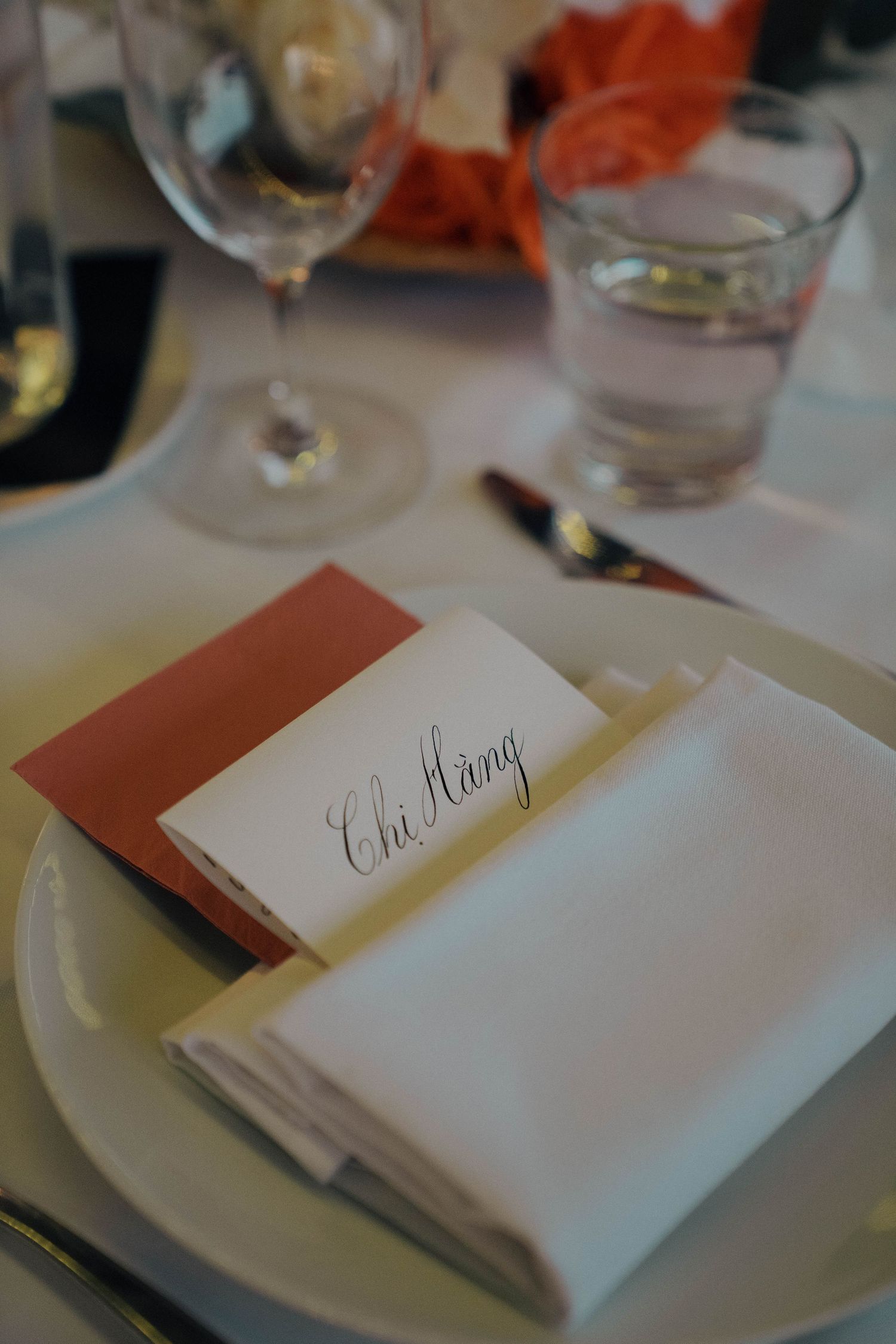 Place settings at a formal dinner table with white napkins and name cards in burgundy red envelopes.