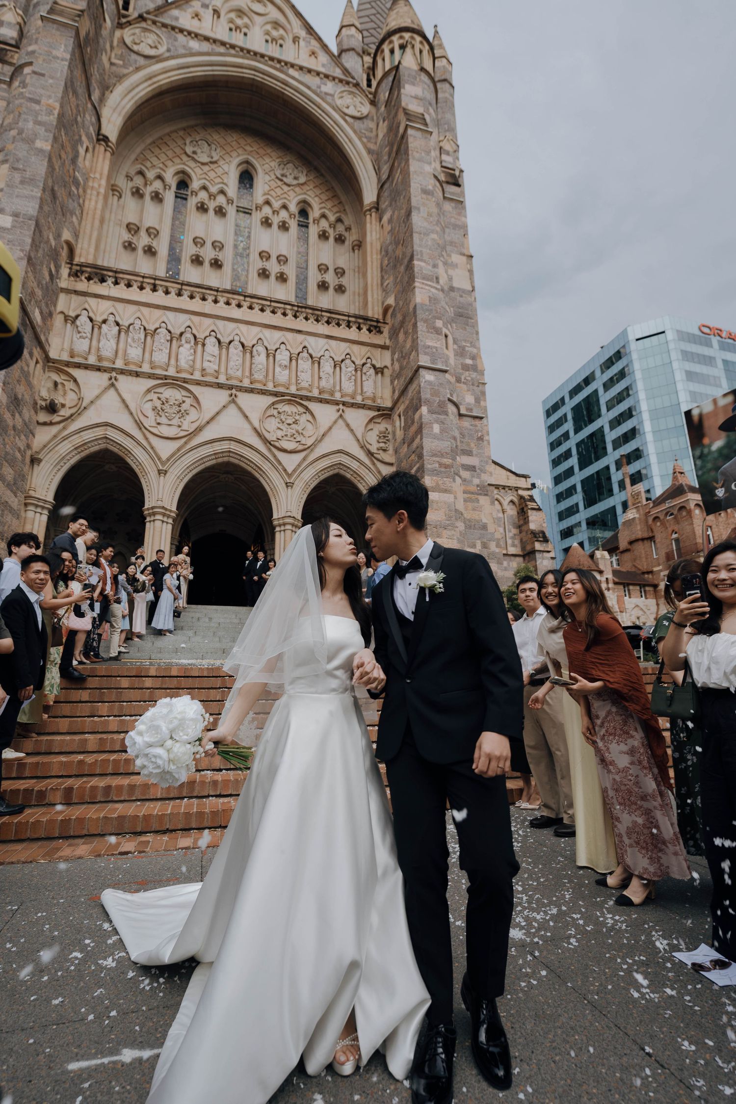 Wedding celebration on church steps with confetti and guests gathered outside ornate cathedral entrance.