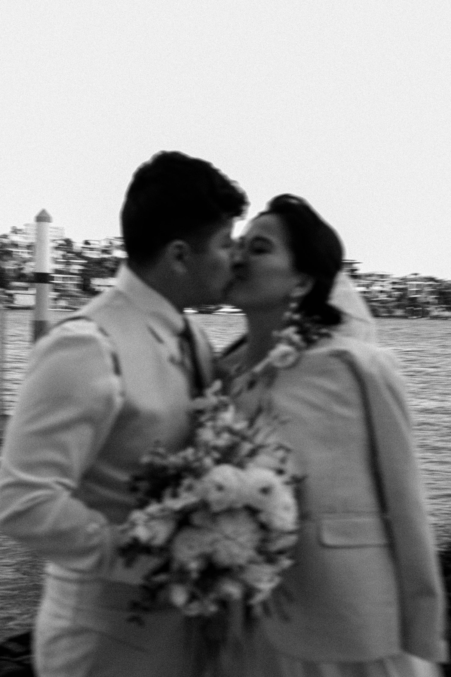 A romantic black and white photo sequence of a couple sharing a kiss at a waterfront wedding ceremony.