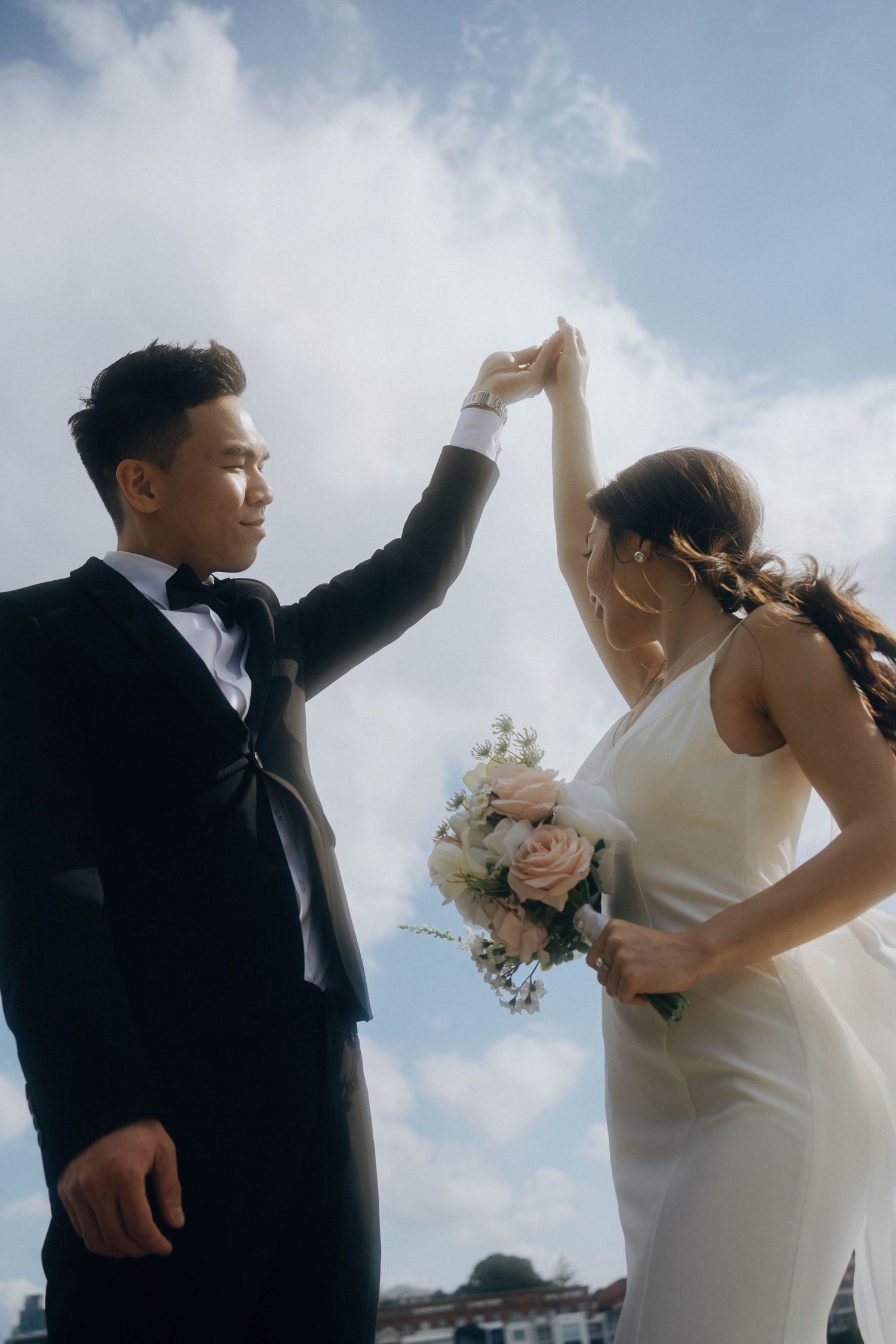 A couple in wedding attire dances joyfully together against a cloudy sky backdrop in a series of candid moments.