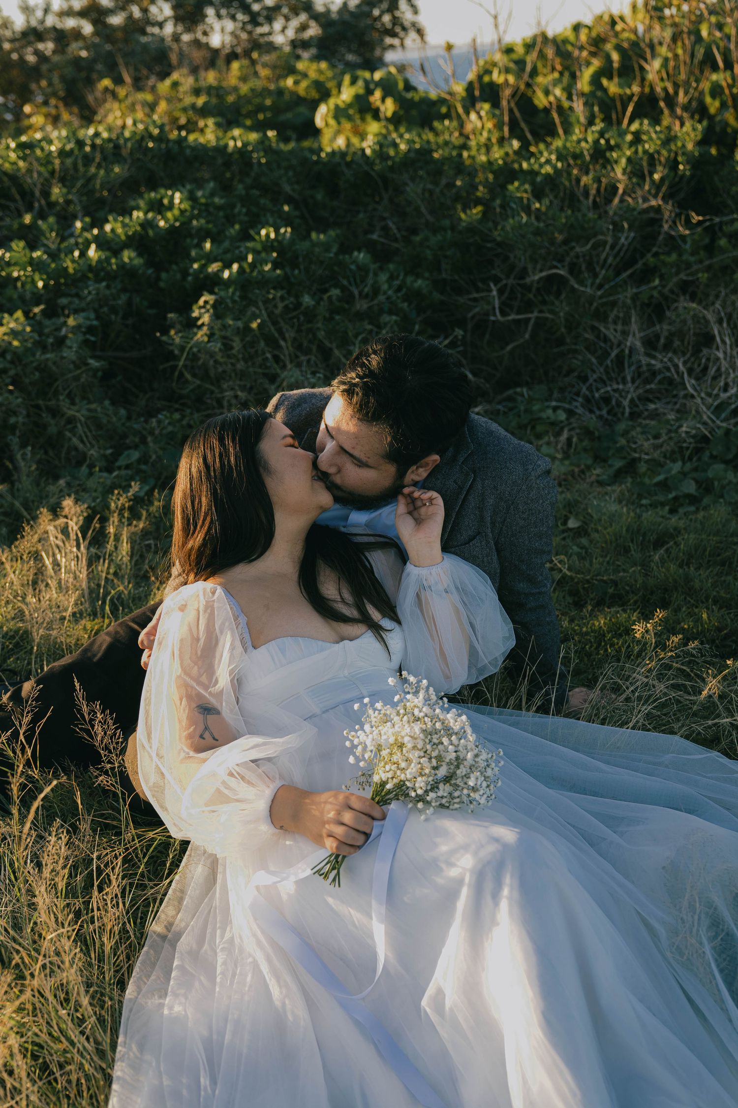 A couple in wedding attire shares romantic moments in a sunlit meadow with wildflowers and tall grass.