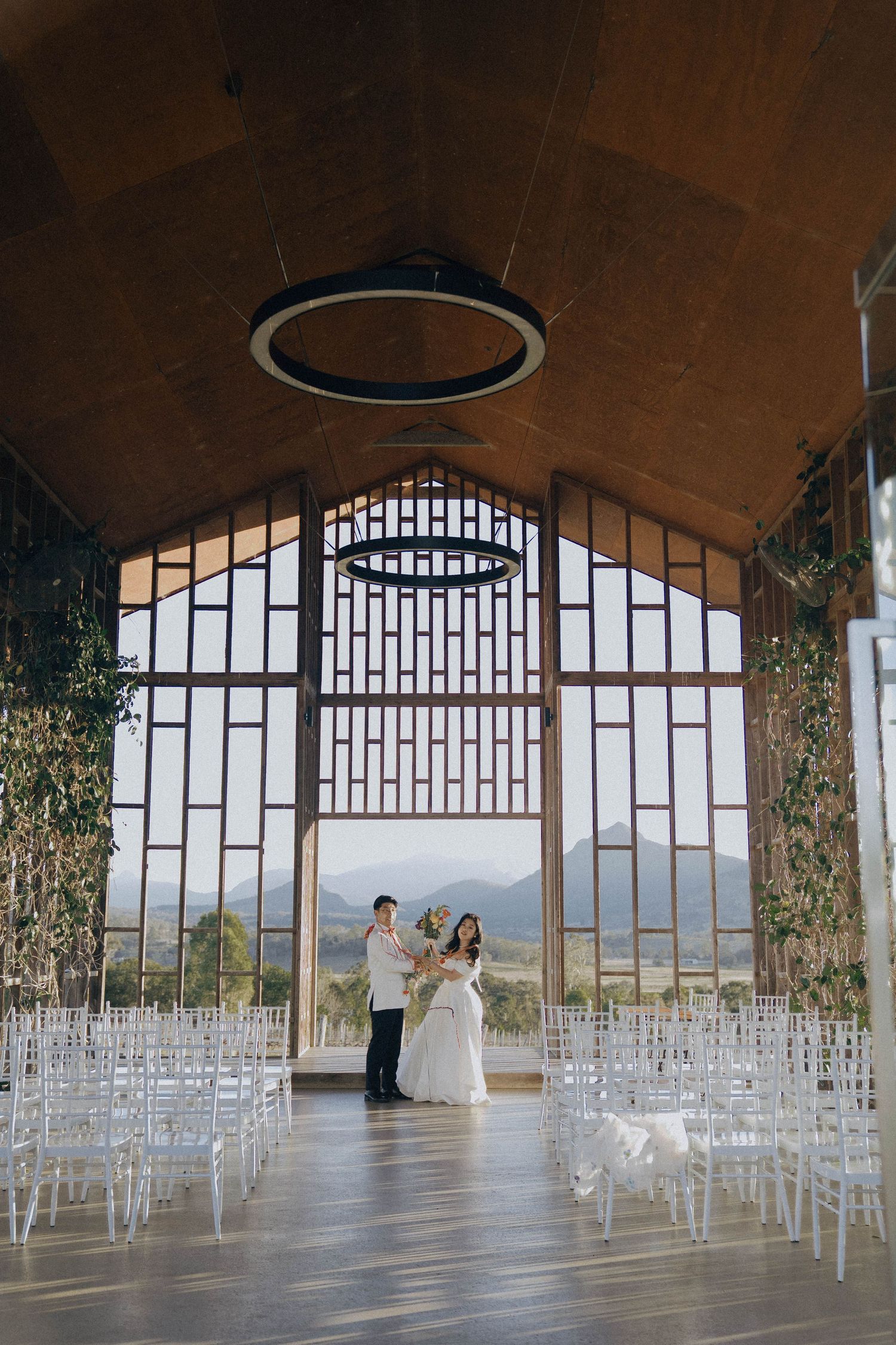 Elegant wedding ceremony setup with rows of white chairs in an arched venue with panoramic mountain views through large windows.