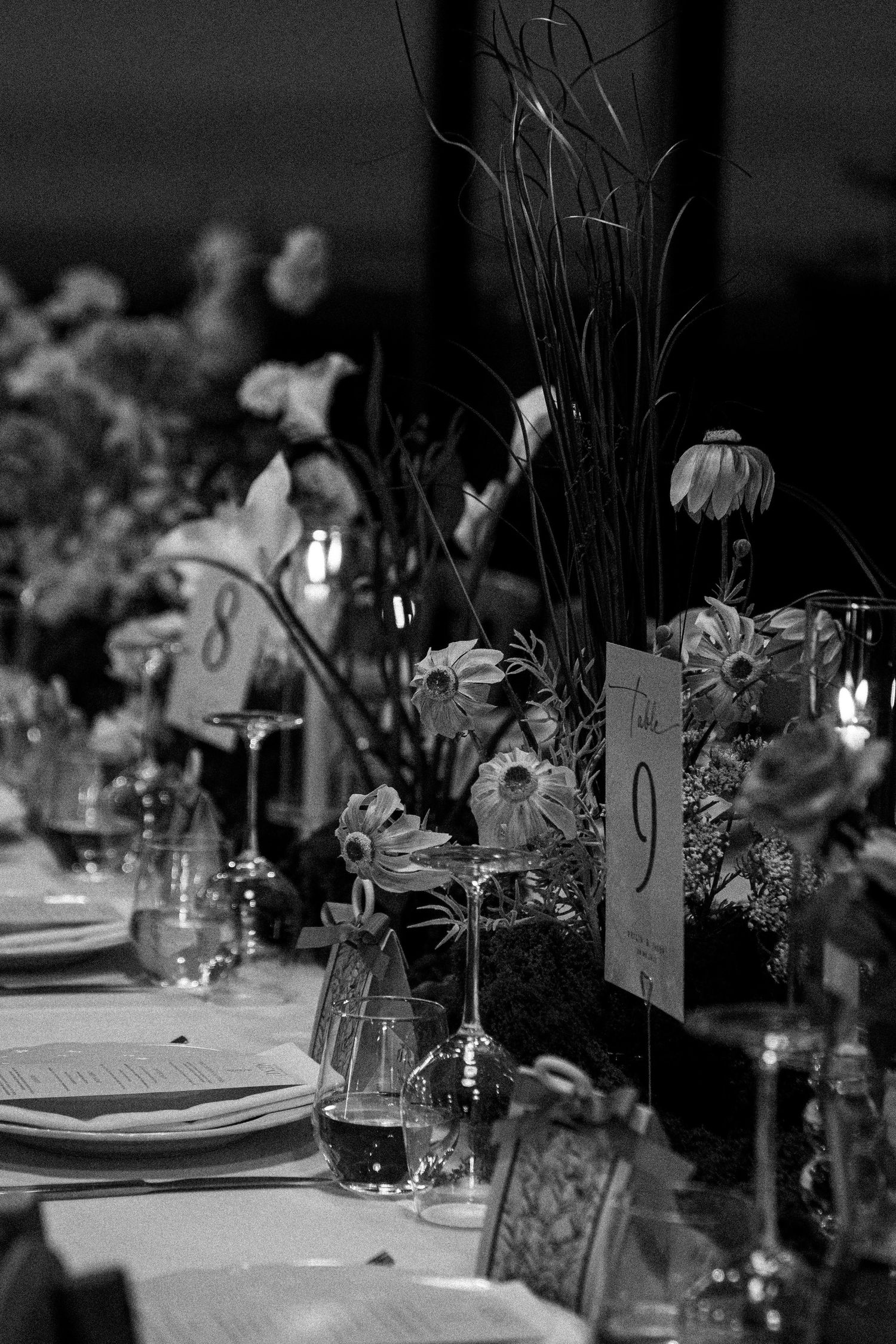 Black and white wedding table settings with place cards and floral centerpieces in a dim lit reception space.