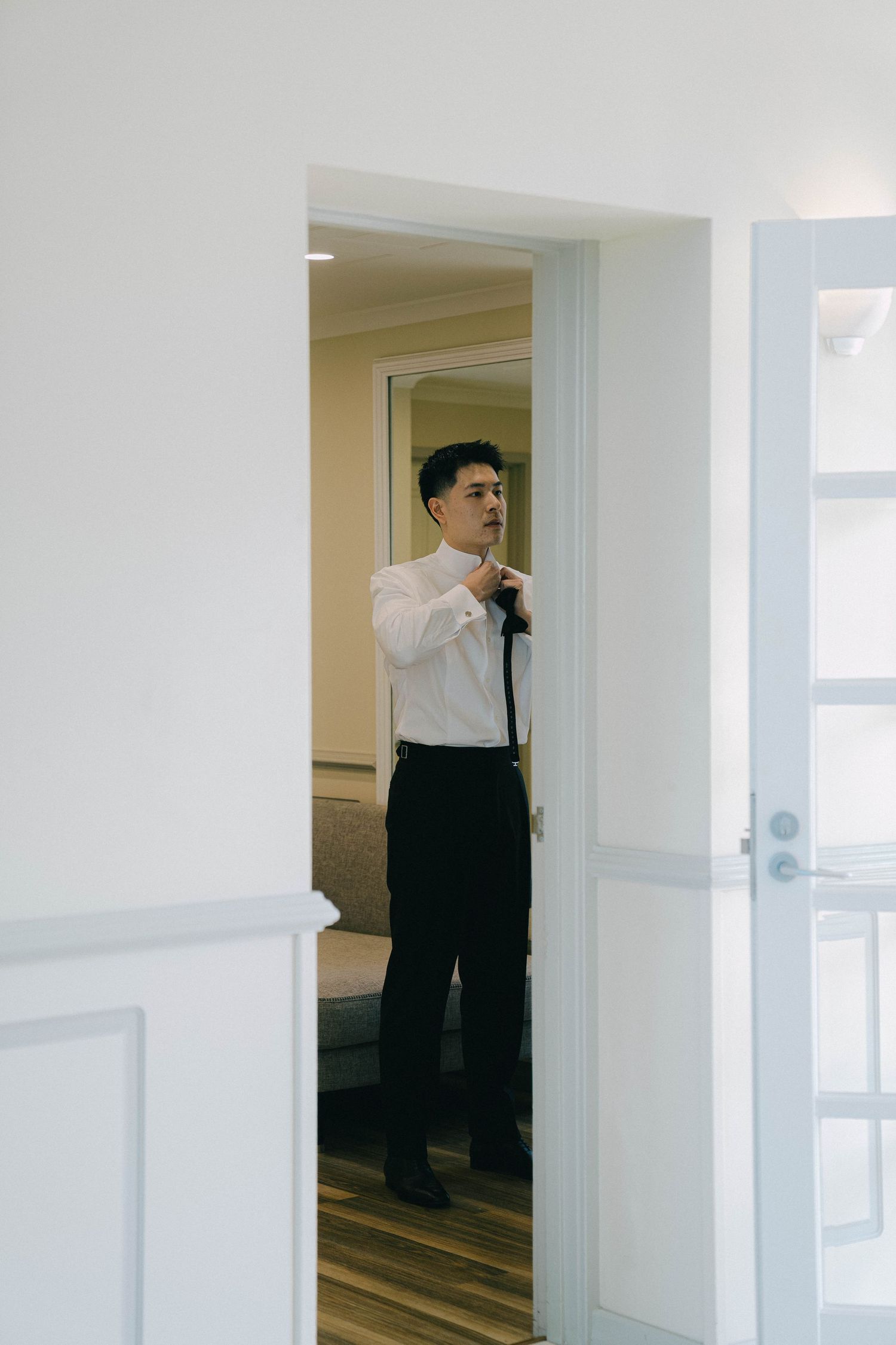 A person in business attire stands in a doorway of a white-walled office hallway.