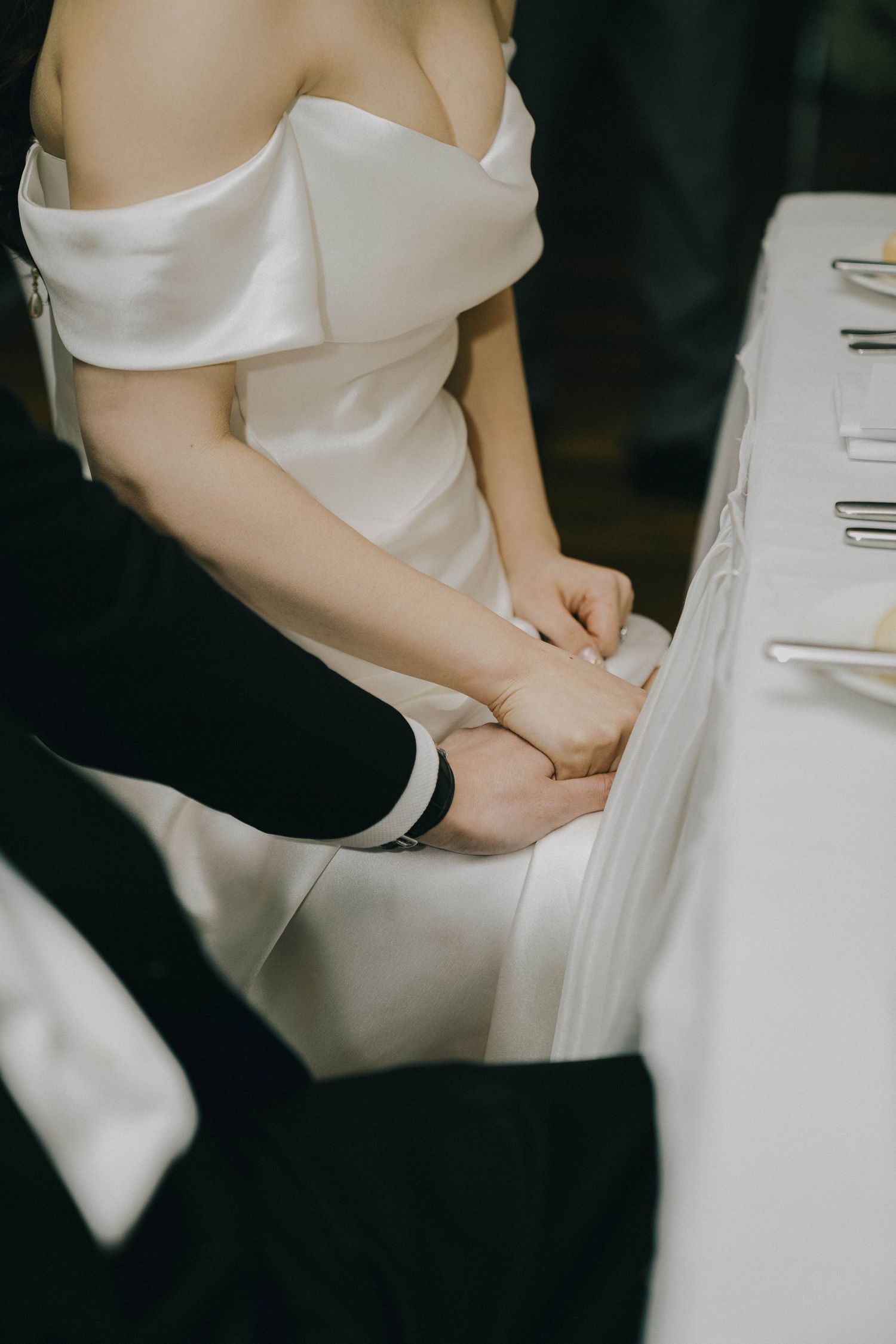 A couple holds hands during their wedding ceremony, with the bride wearing an elegant off-shoulder white dress.