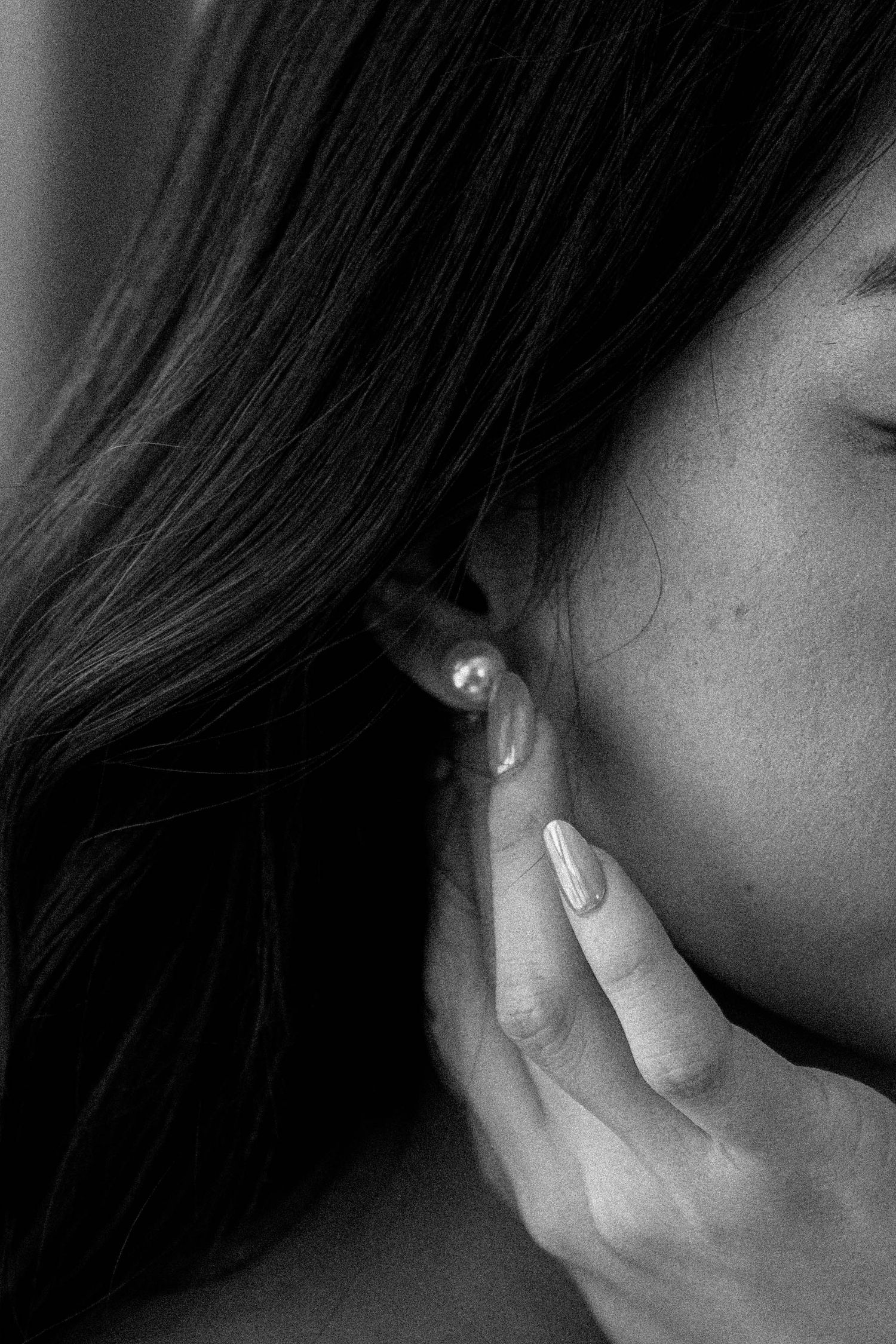 Close-up black and white photo sequence showing a hand gently touching an ear with a small stud earring.