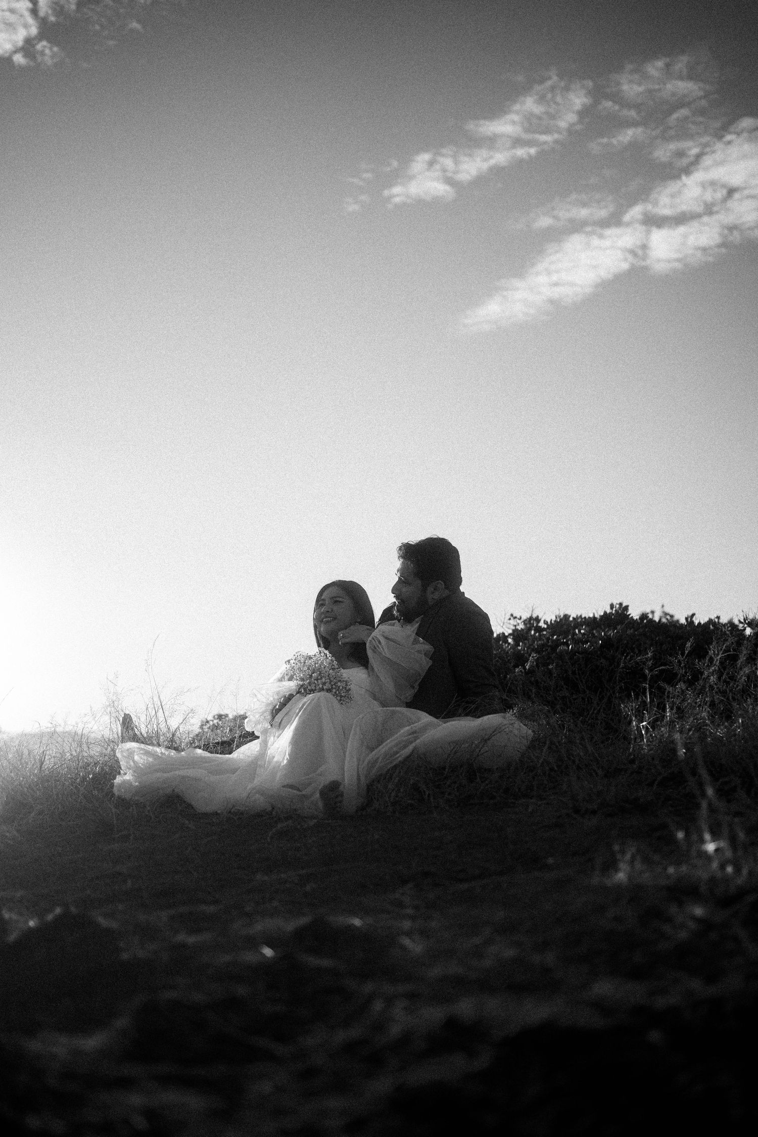 A sequence of black and white silhouettes showing two people laying down on a hill against a cloudy sky.