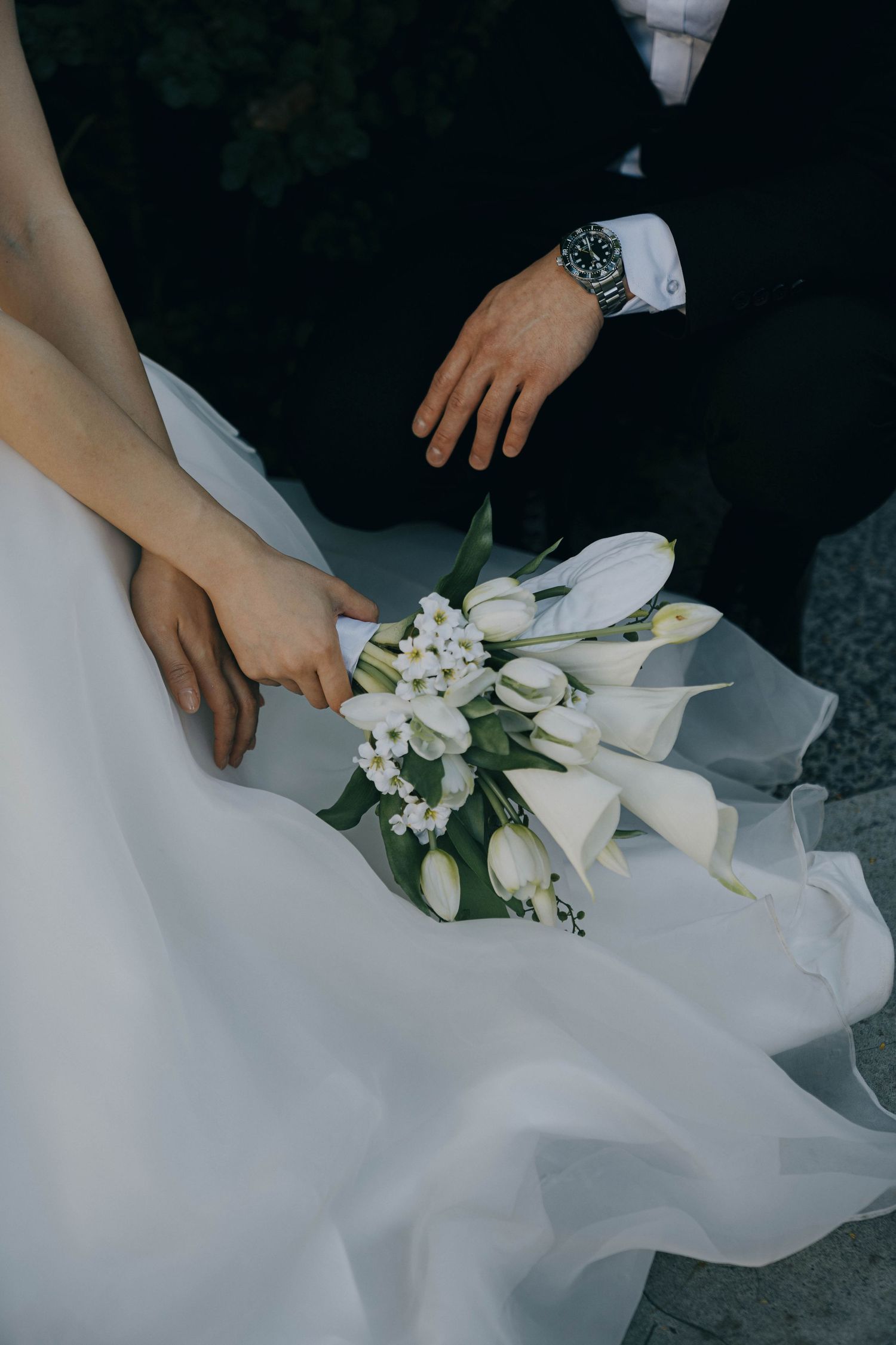 Delicate white flowers and tulle fabric details from a wedding dress being arranged by hands.