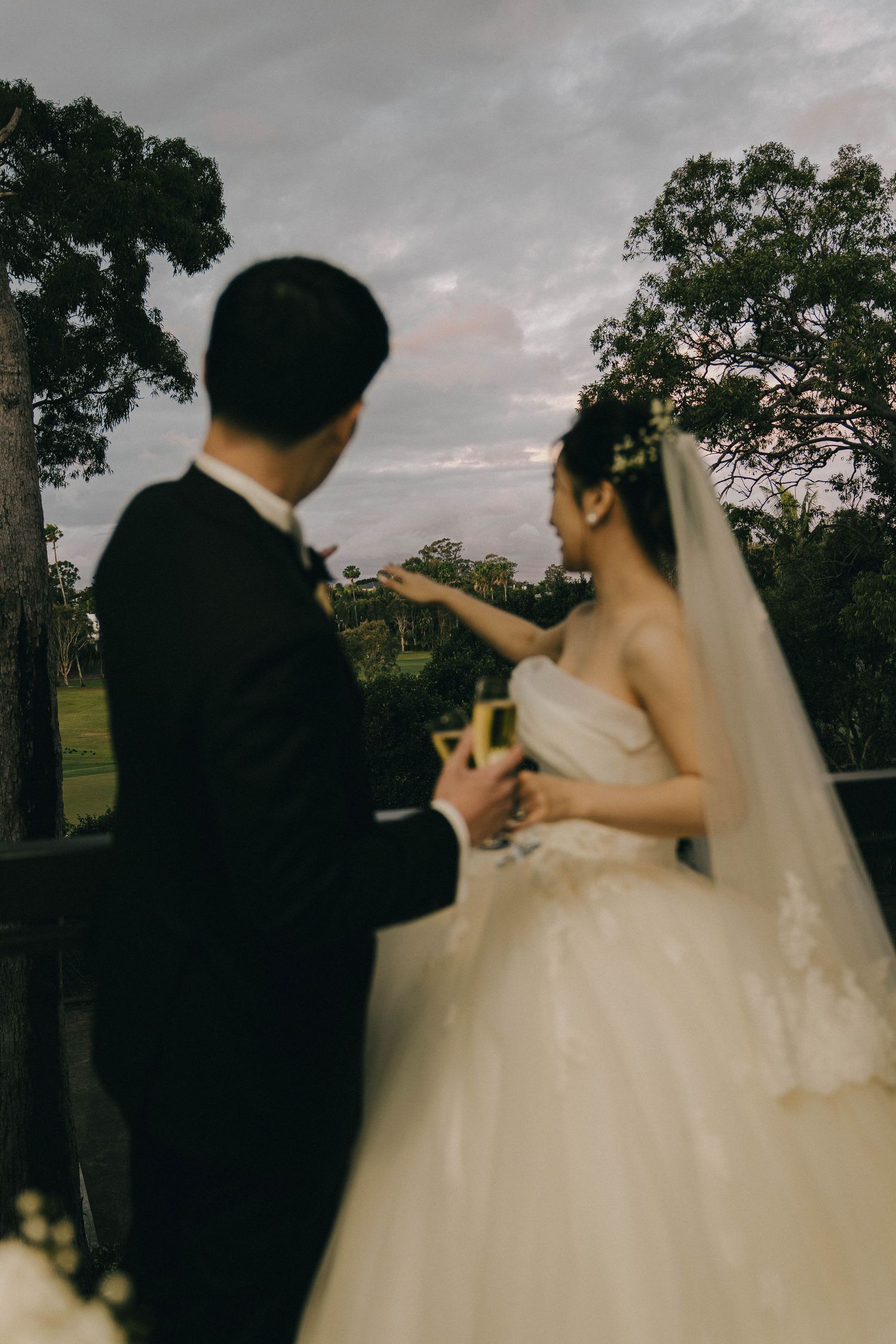 A couple in wedding attire dancing together at sunset with trees in the background.