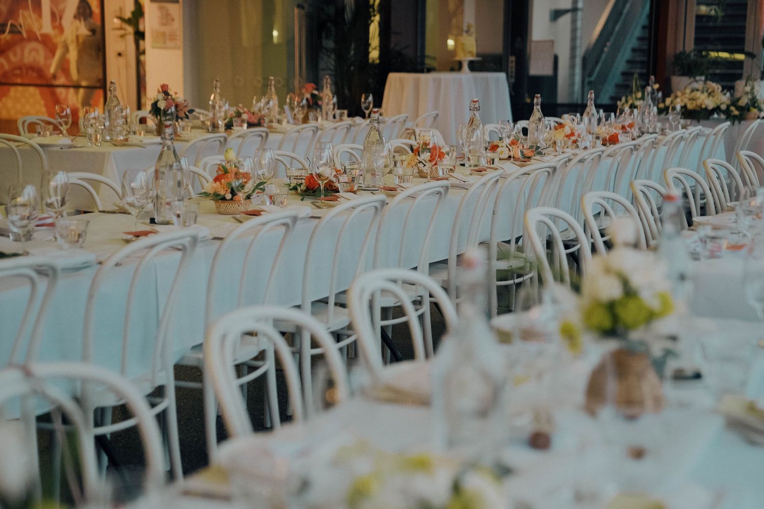 Long rows of elegant white dining tables set for a formal wedding reception with floral centerpieces and place settings.