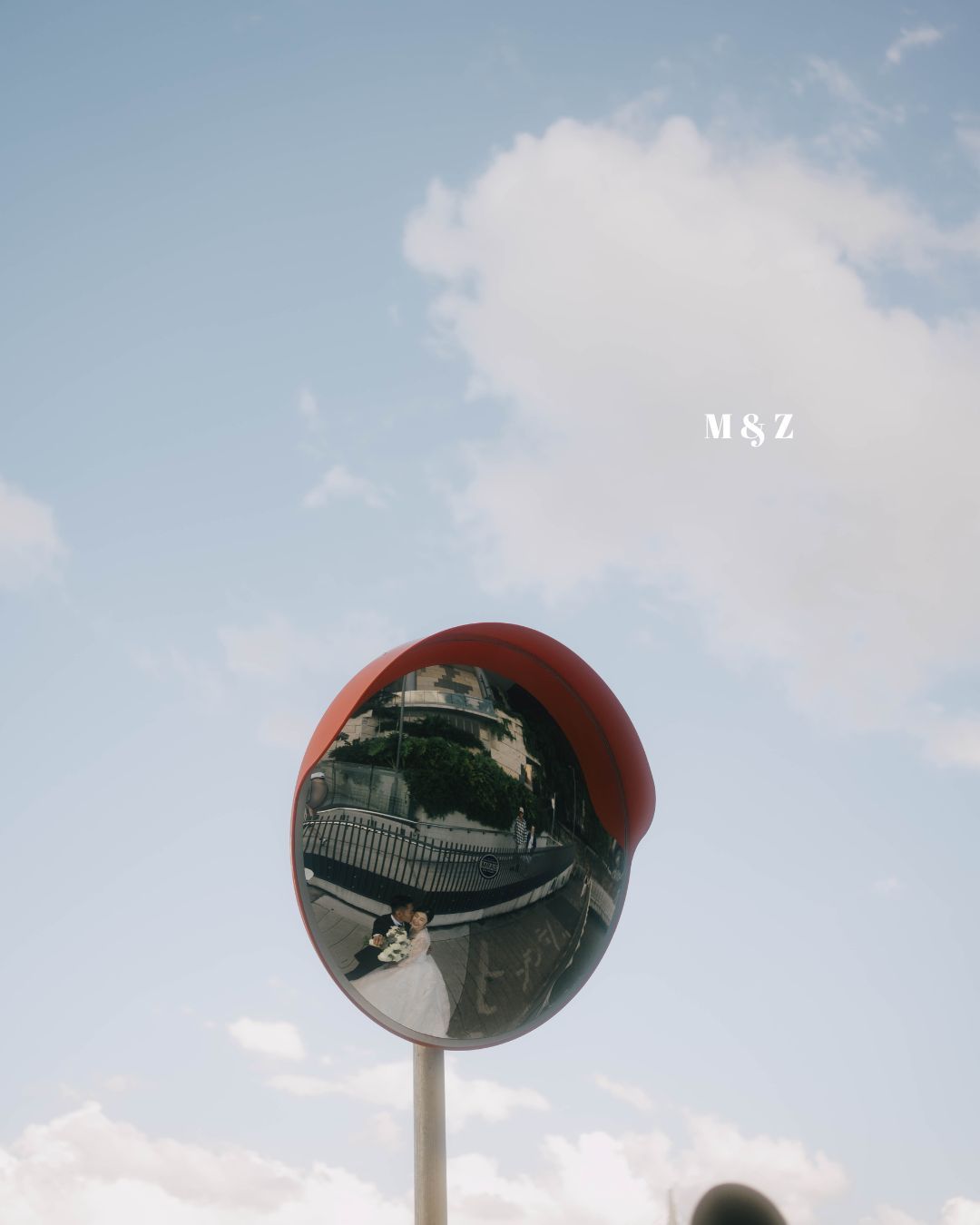 A red convex security mirror mounted on a pole reflects buildings and sky against a light blue background.
