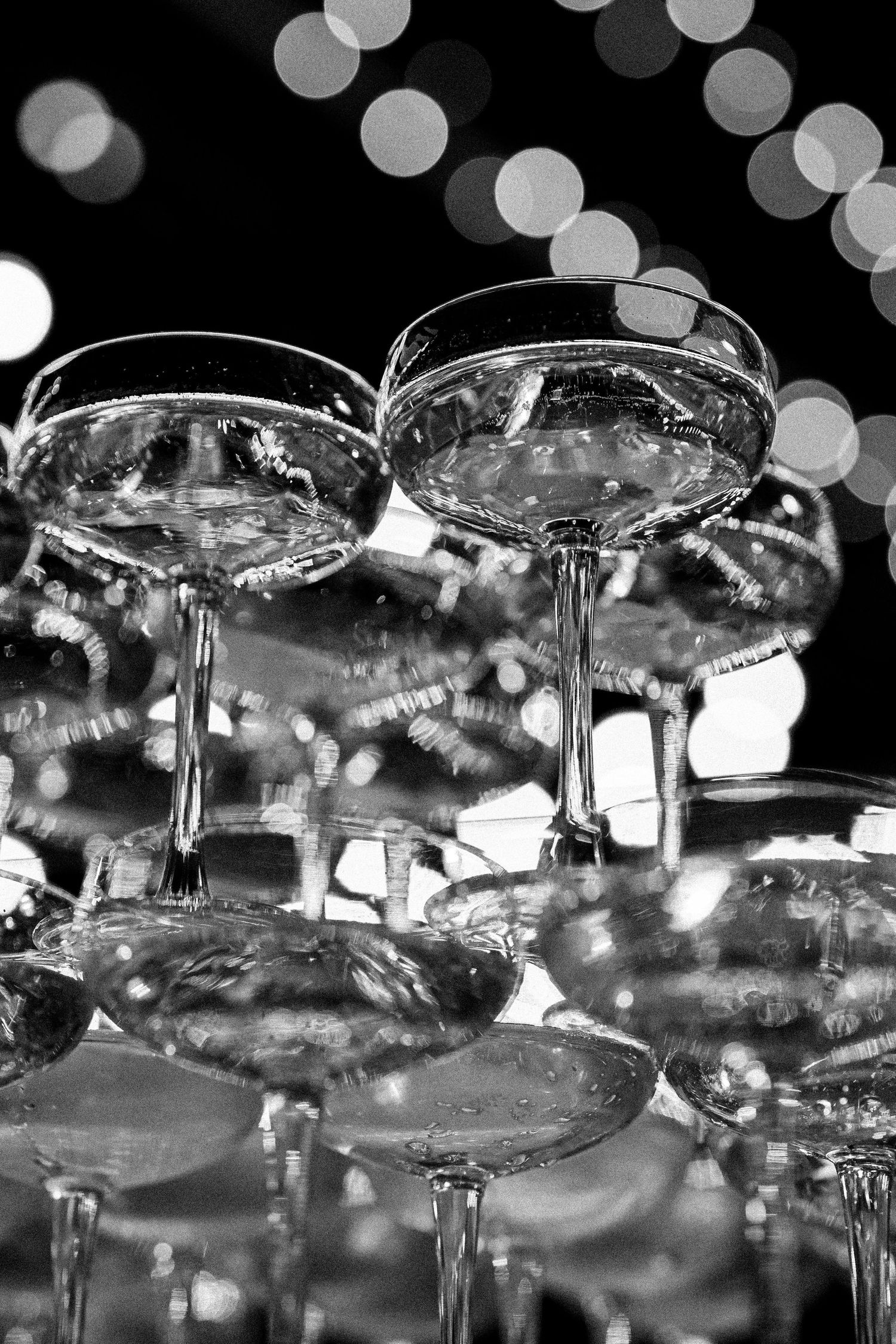 Crystal champagne glasses stacked in a pyramid formation with glittering bokeh lights in the background.