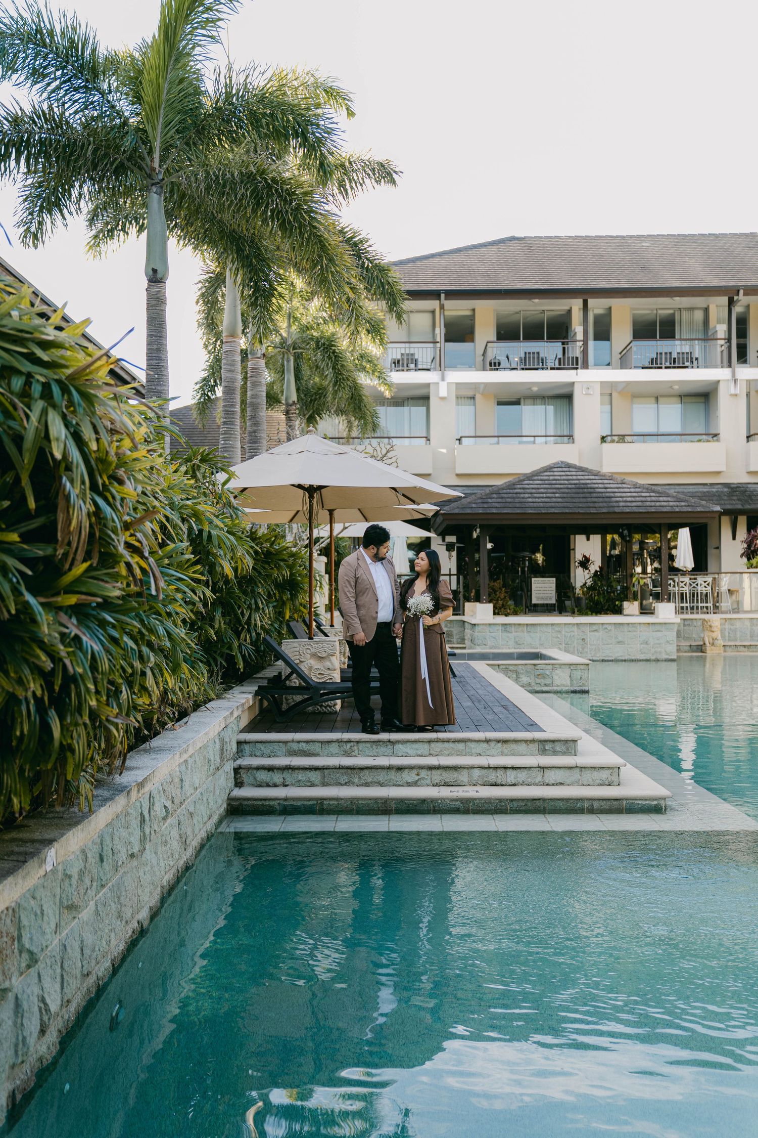 Luxury modern swimming pool with palm trees and contemporary architecture features multiple connected sections.