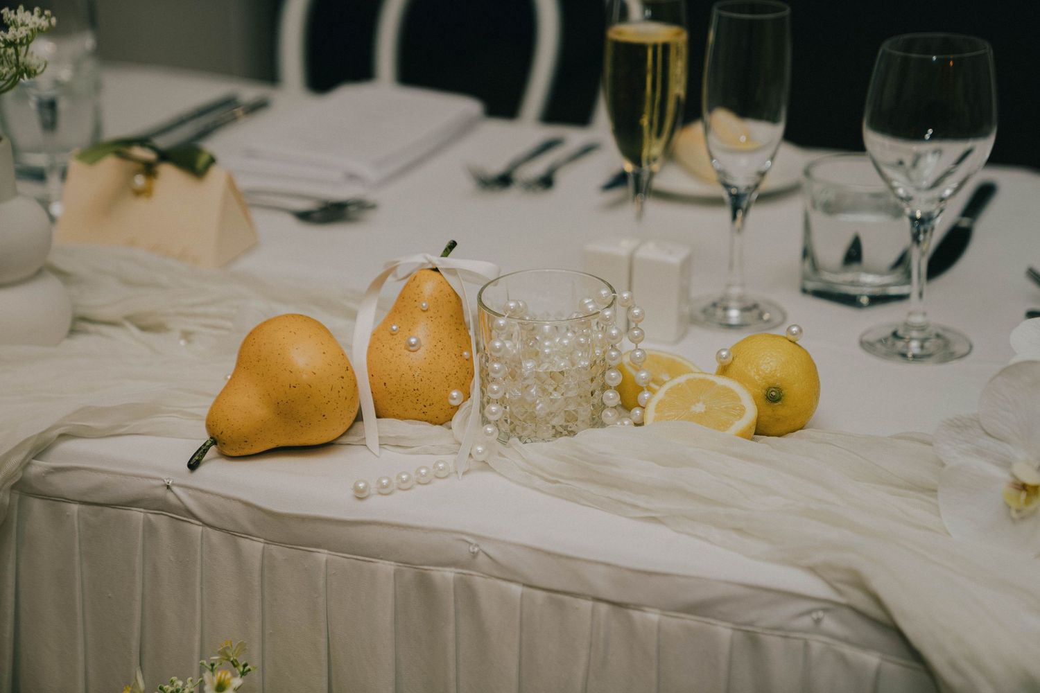 Elegant white tablecloth dining setup with fresh pears and wine glasses at a formal event.