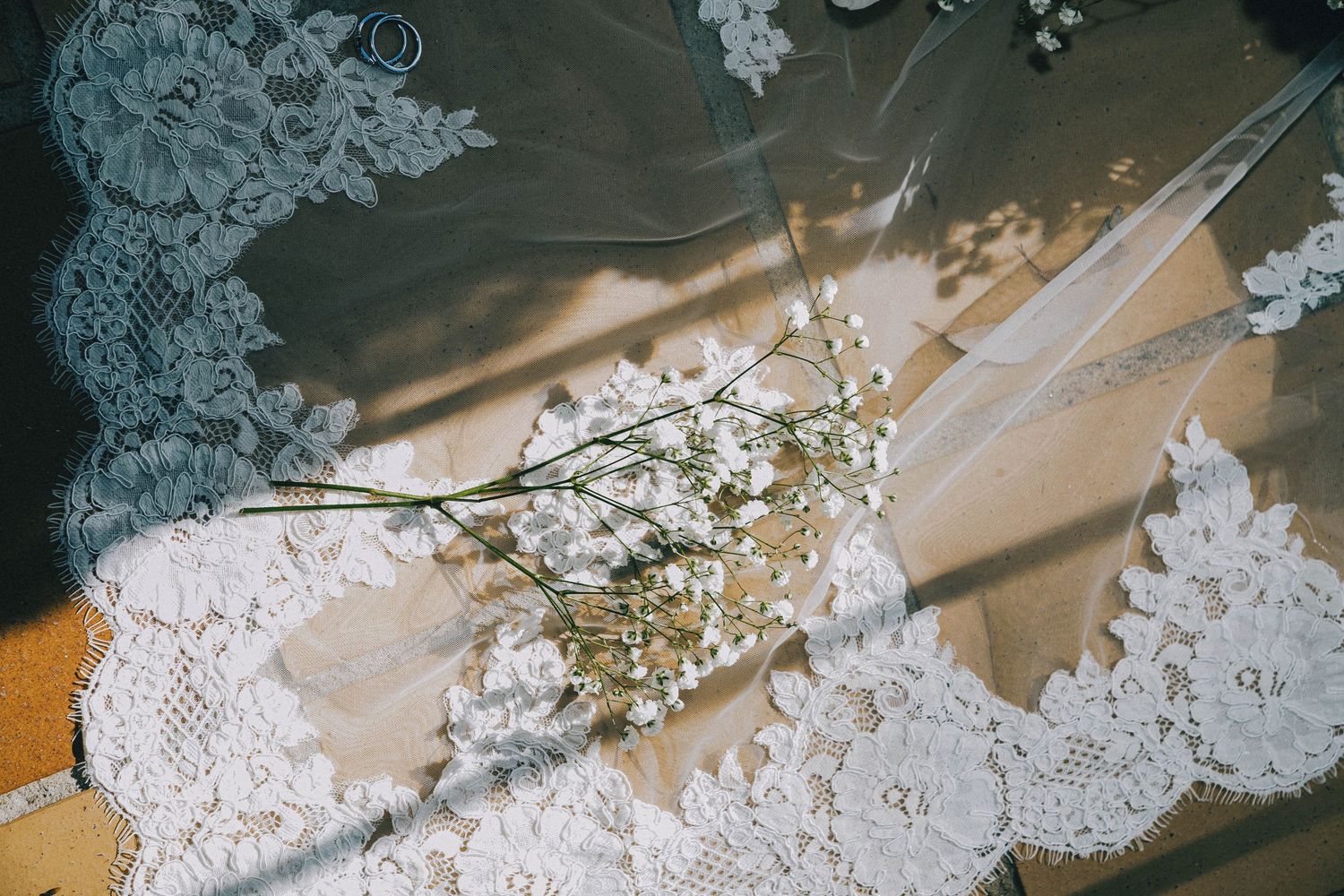 Delicate white lace wedding dress details with floral embroidery patterns and beading against a soft neutral background.