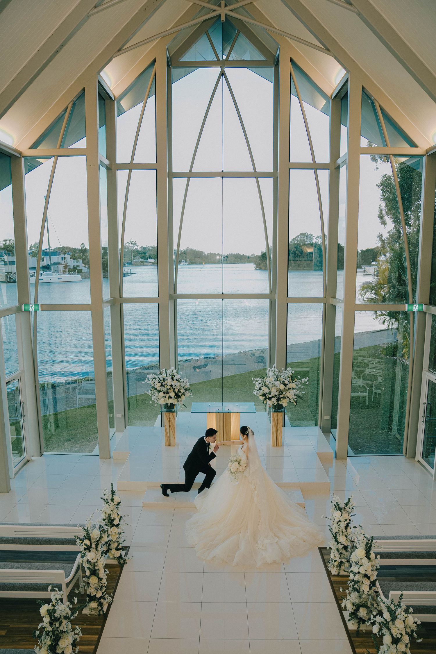 A panoramic series of wedding photos in a modern glass chapel overlooking a waterfront view with white floral arrangements.