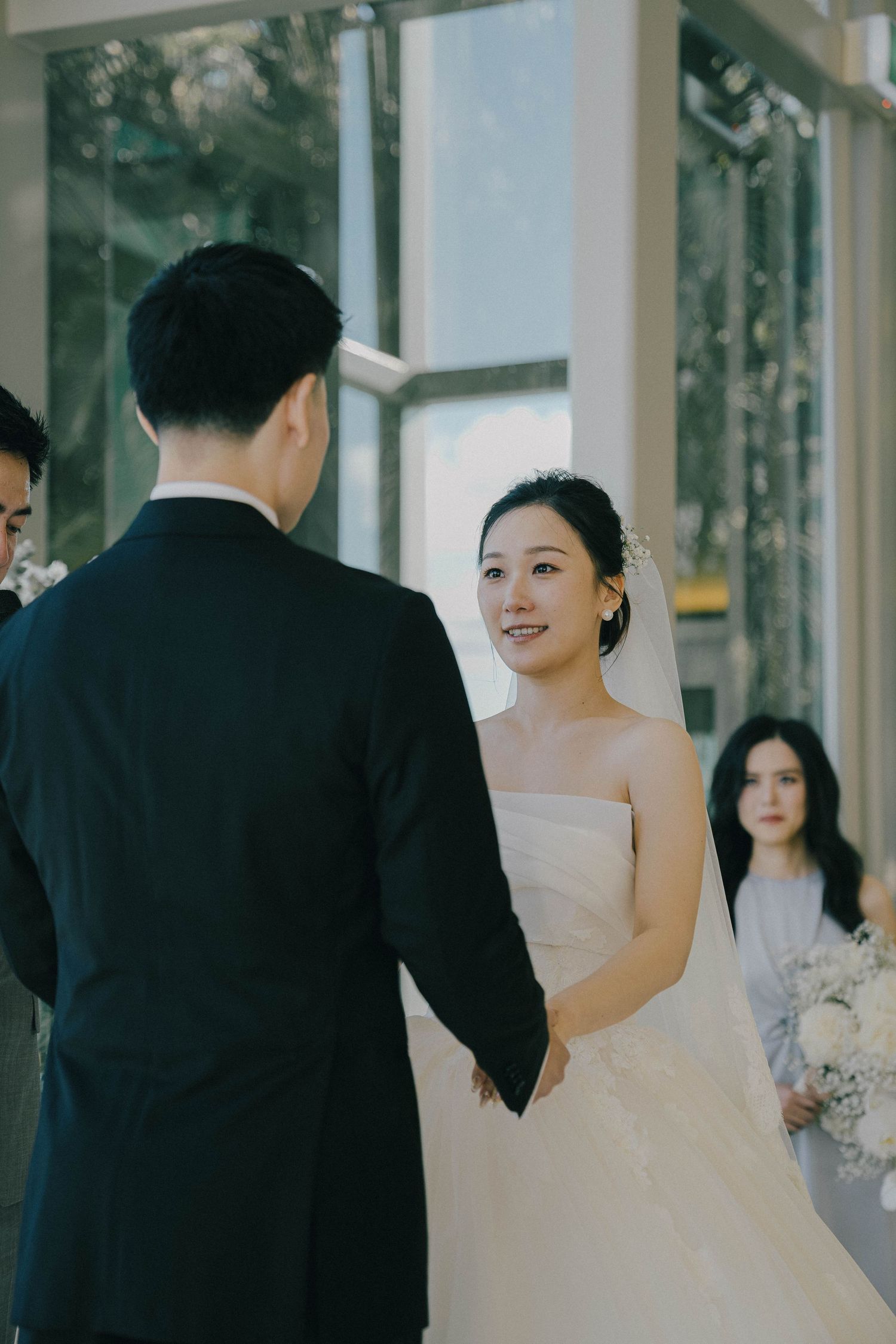 A bride in a white strapless wedding gown and groom in black suit share intimate moments in an elegant venue hallway.