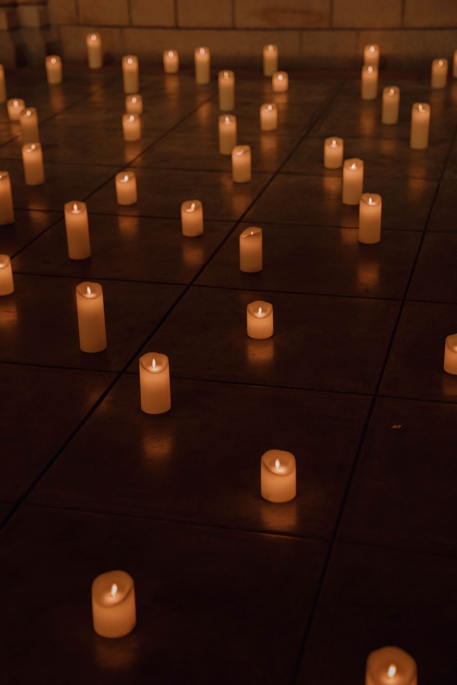 Glowing white candles arranged in a grid pattern create a serene and atmospheric display in darkness.