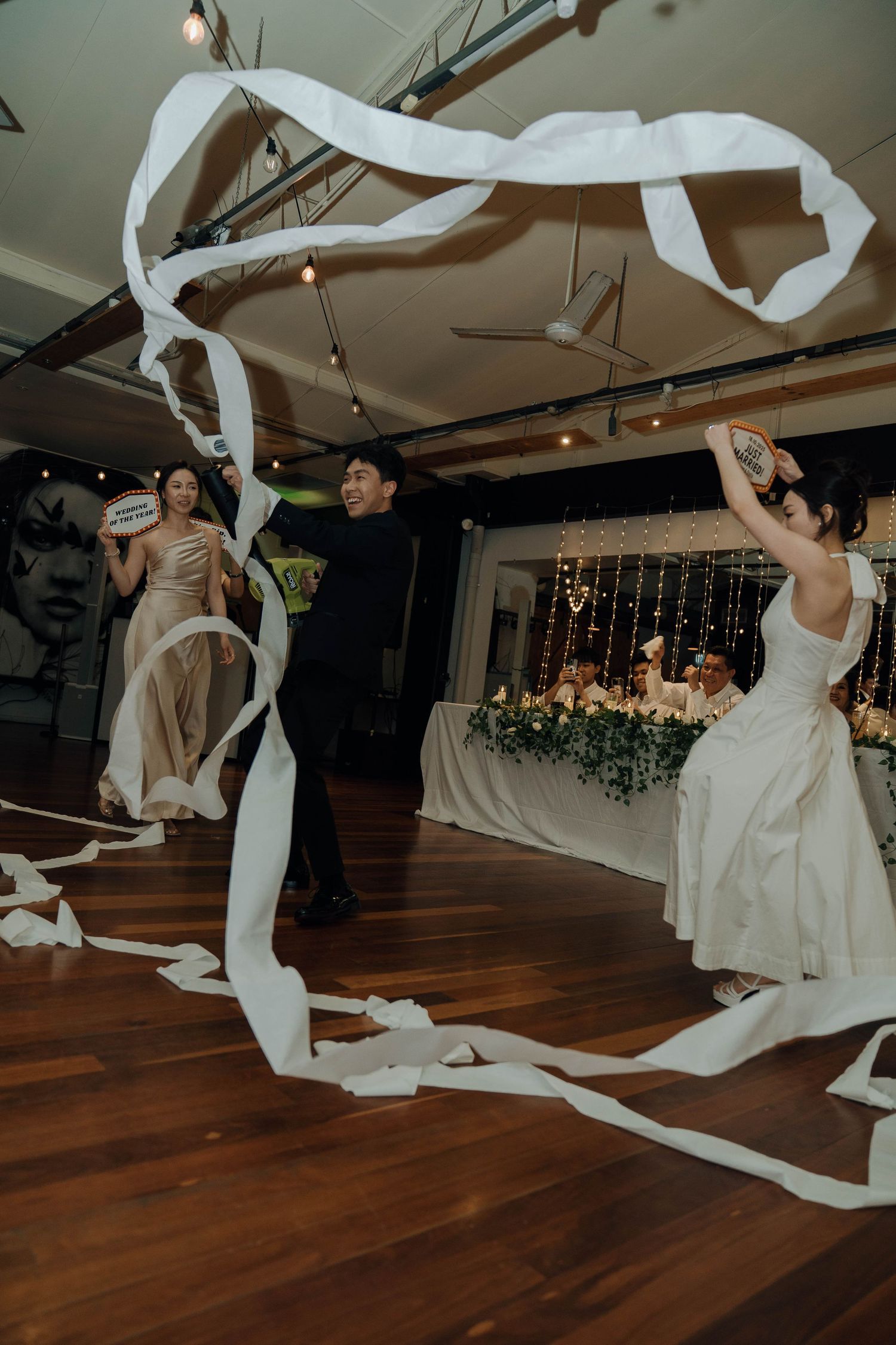 A sequence of wedding dancers in white dresses twirling with flowing fabric ribbons on a wooden dance floor.