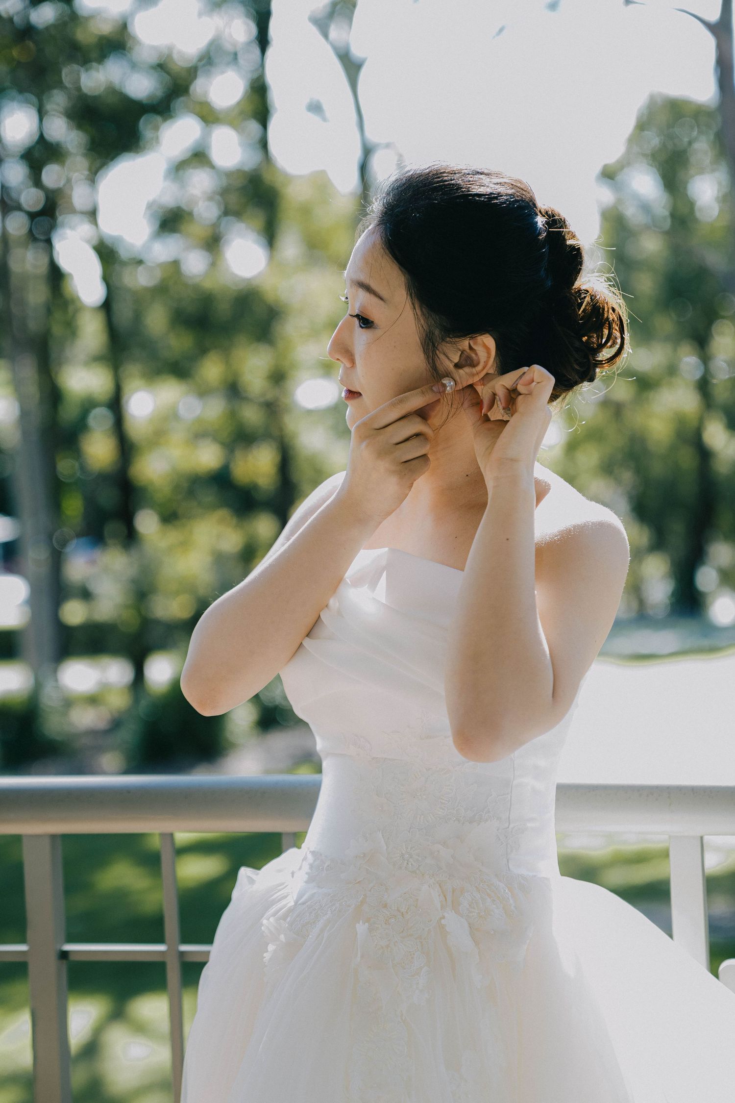 A person in a white dress stands outdoors covering their mouth with their hand in a candid moment.