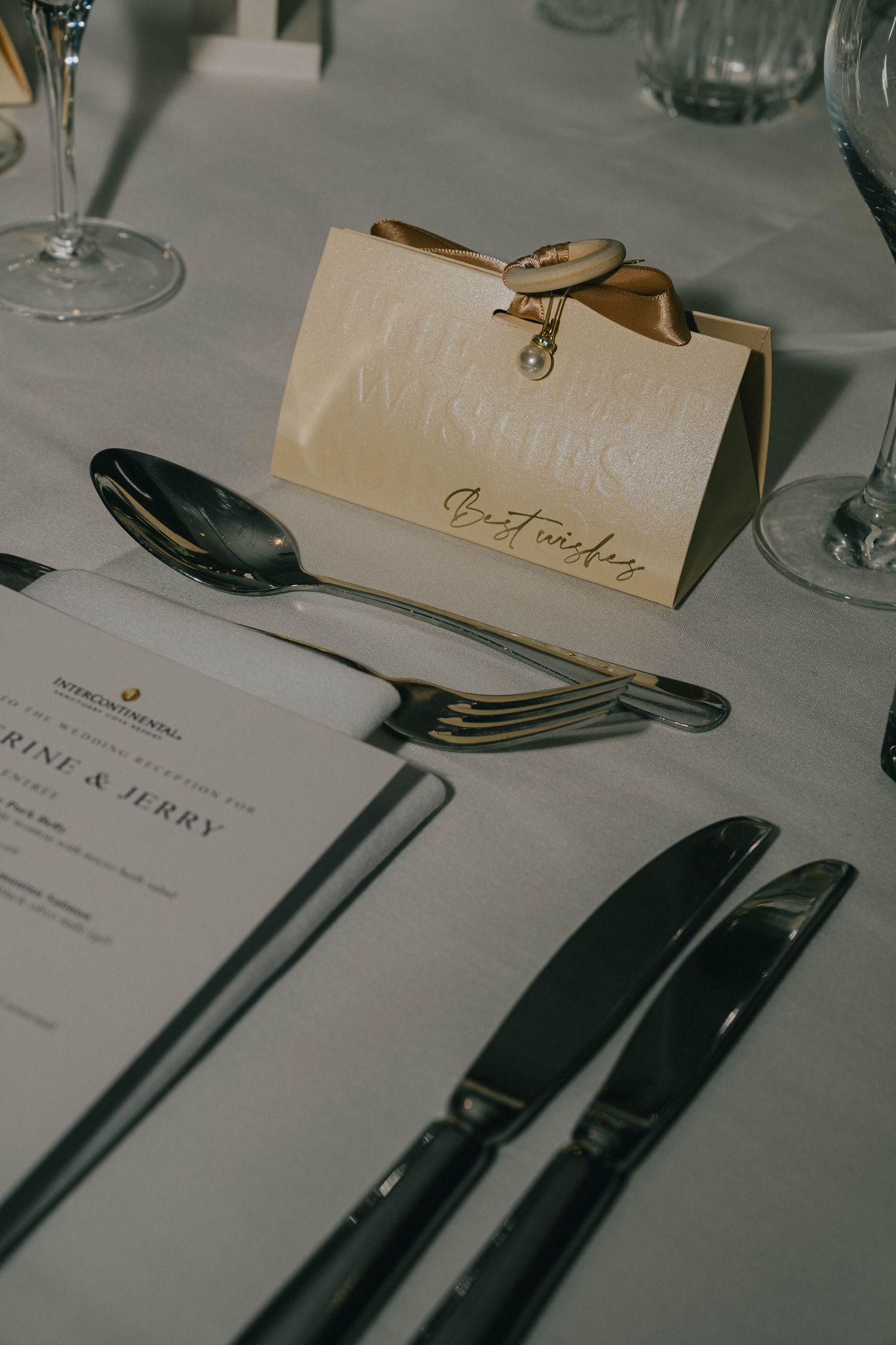 Place settings at an elegant dinner table with formal silverware, name cards and menu cards arranged on white linens.