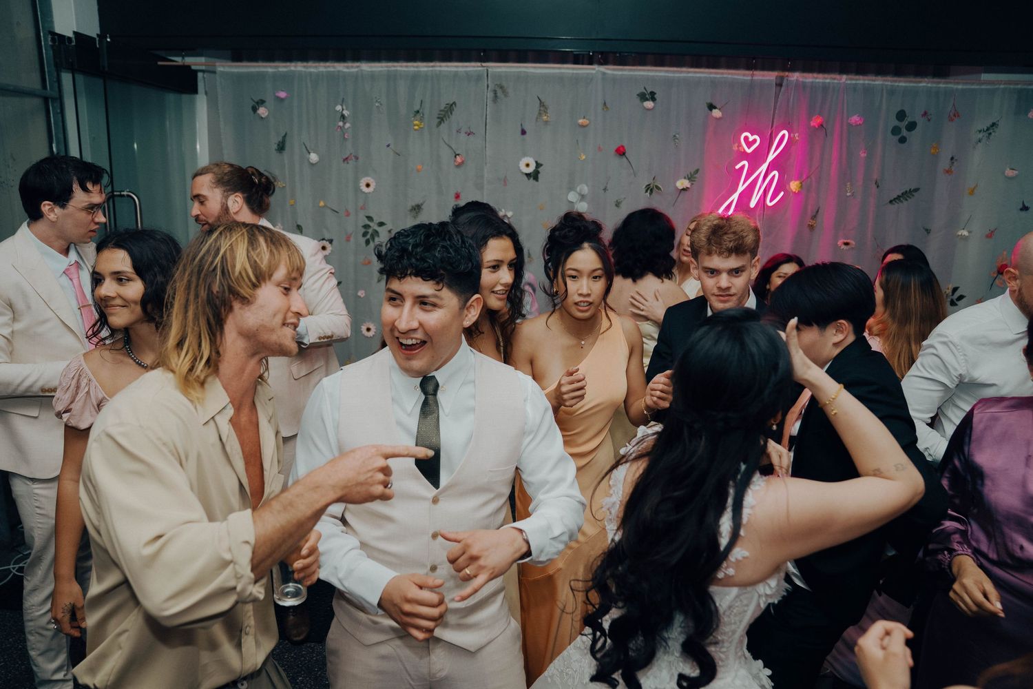 Wedding reception guests dancing and celebrating together under pink neon lighting.