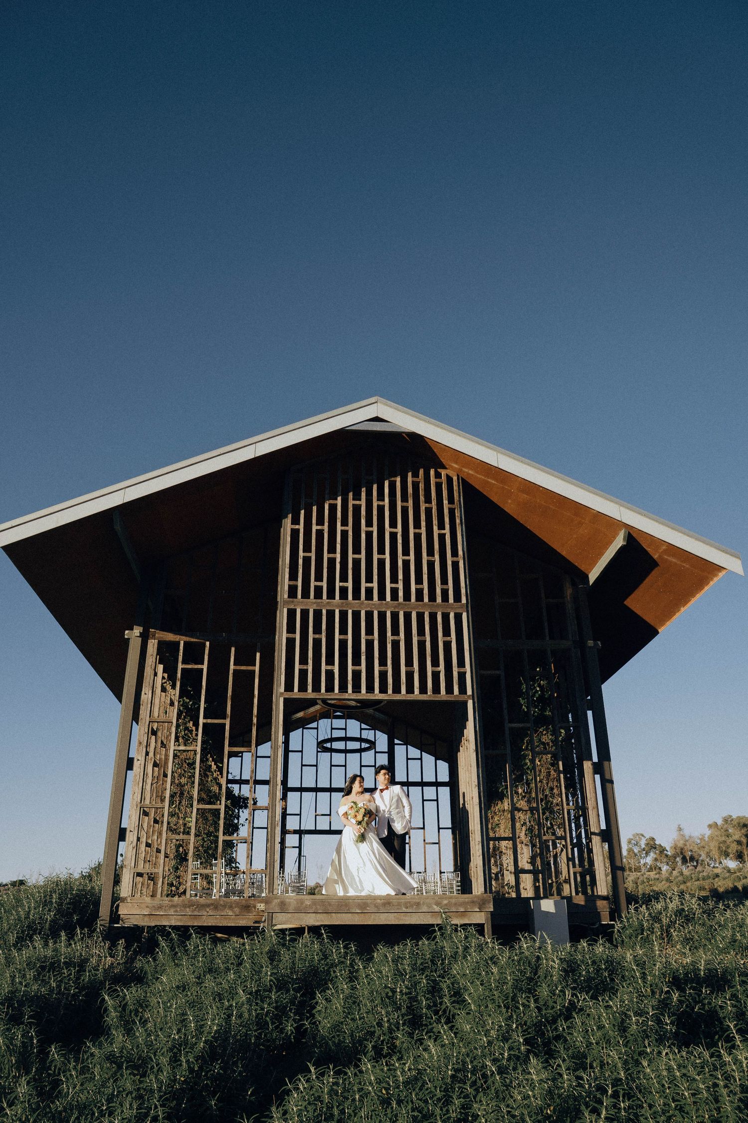 A modern wooden chapel with slatted walls sits on a hilltop against a blue sky in a panoramic sequence of views.
